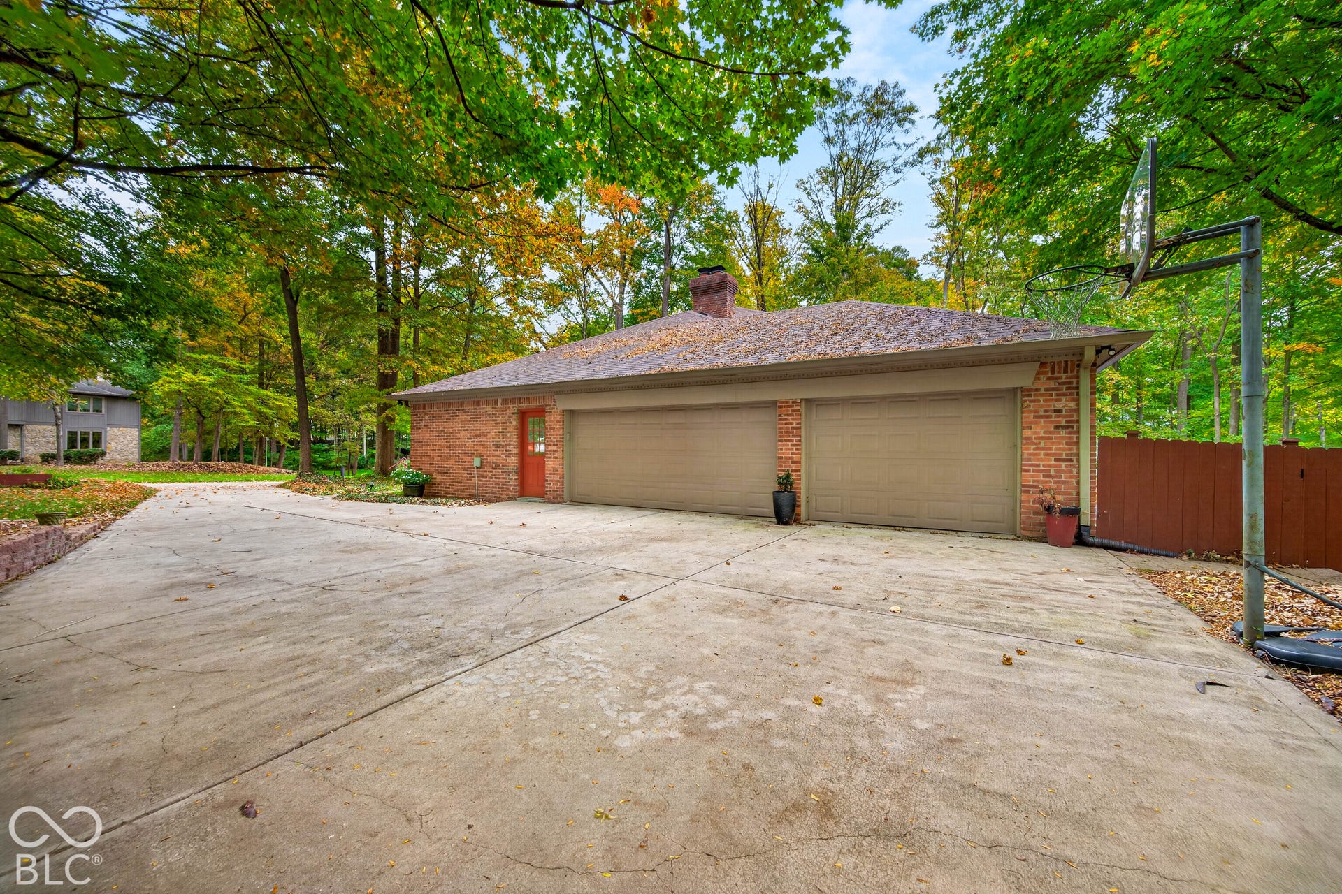 Detached brick garage featuring a concrete driveway, dual garage doors, a masonry chimney, and mature perimeter trees