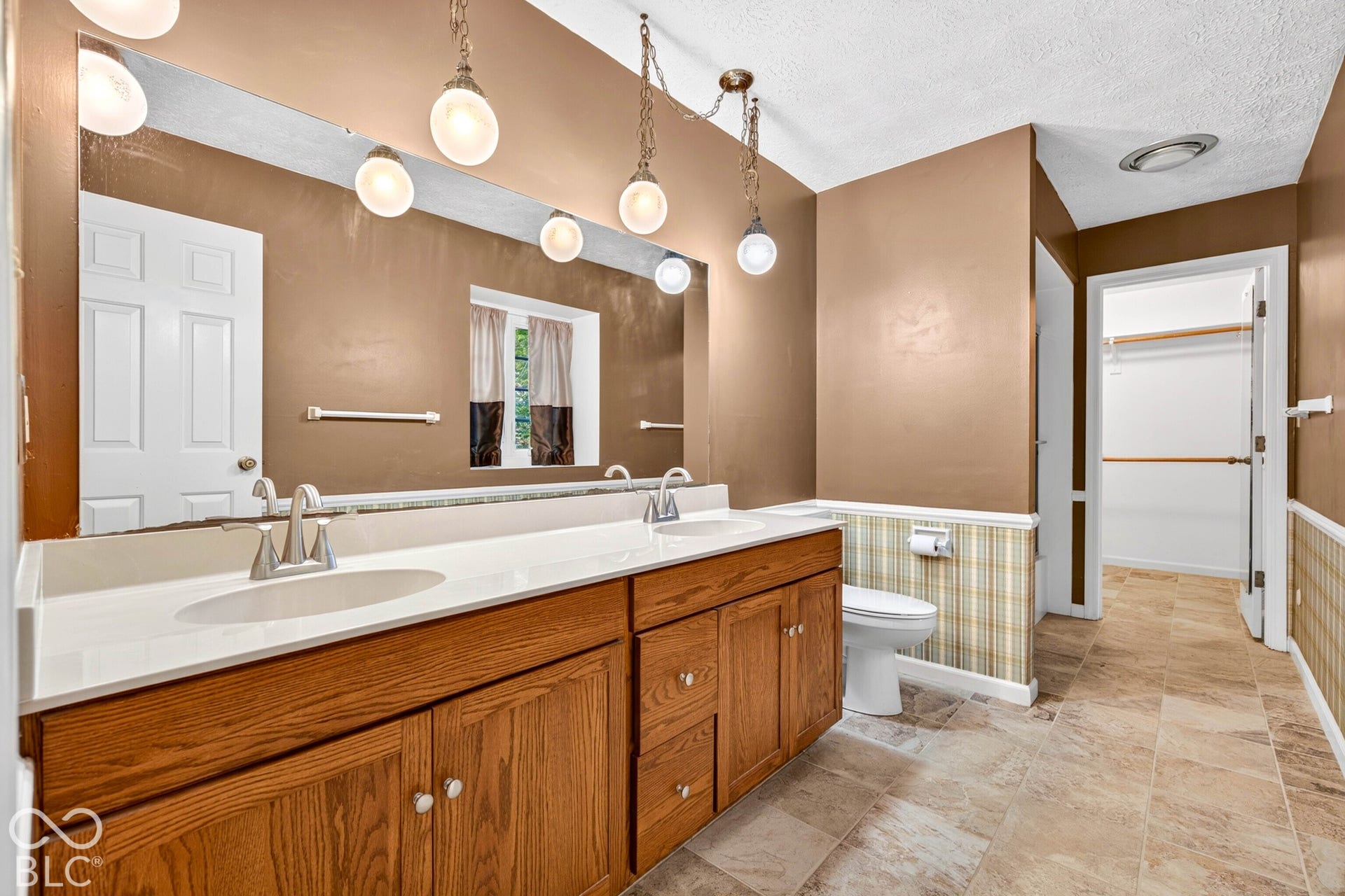 Double vanity featuring wood cabinetry, a solid surface countertop with integrated dual sinks, a large wall-mounted mirror, and multi-light pendant fixtures