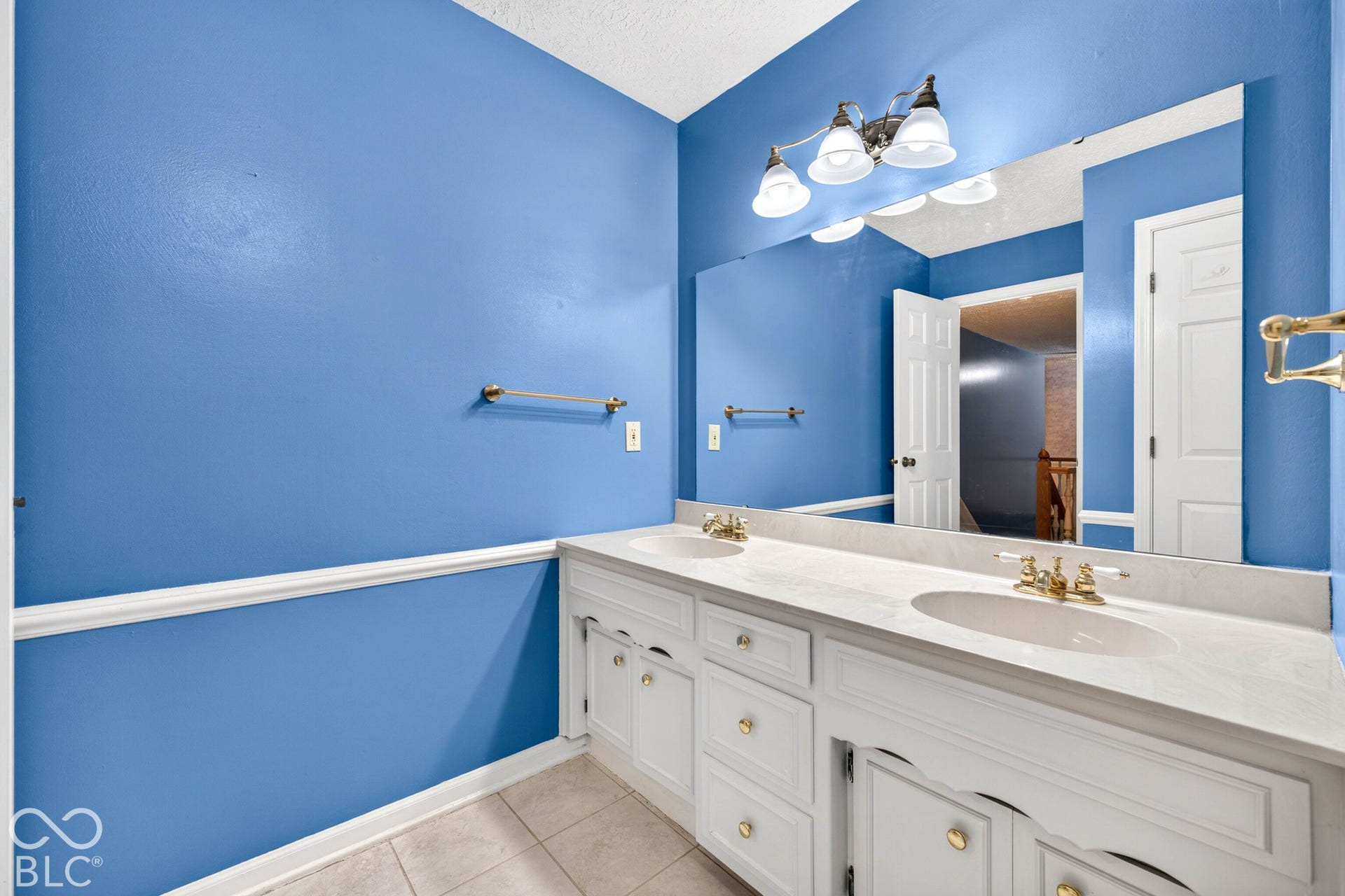 Dual-sink vanity with a countertop, expansive wall-to-wall mirror, brass-finish hardware, and three-light fixture