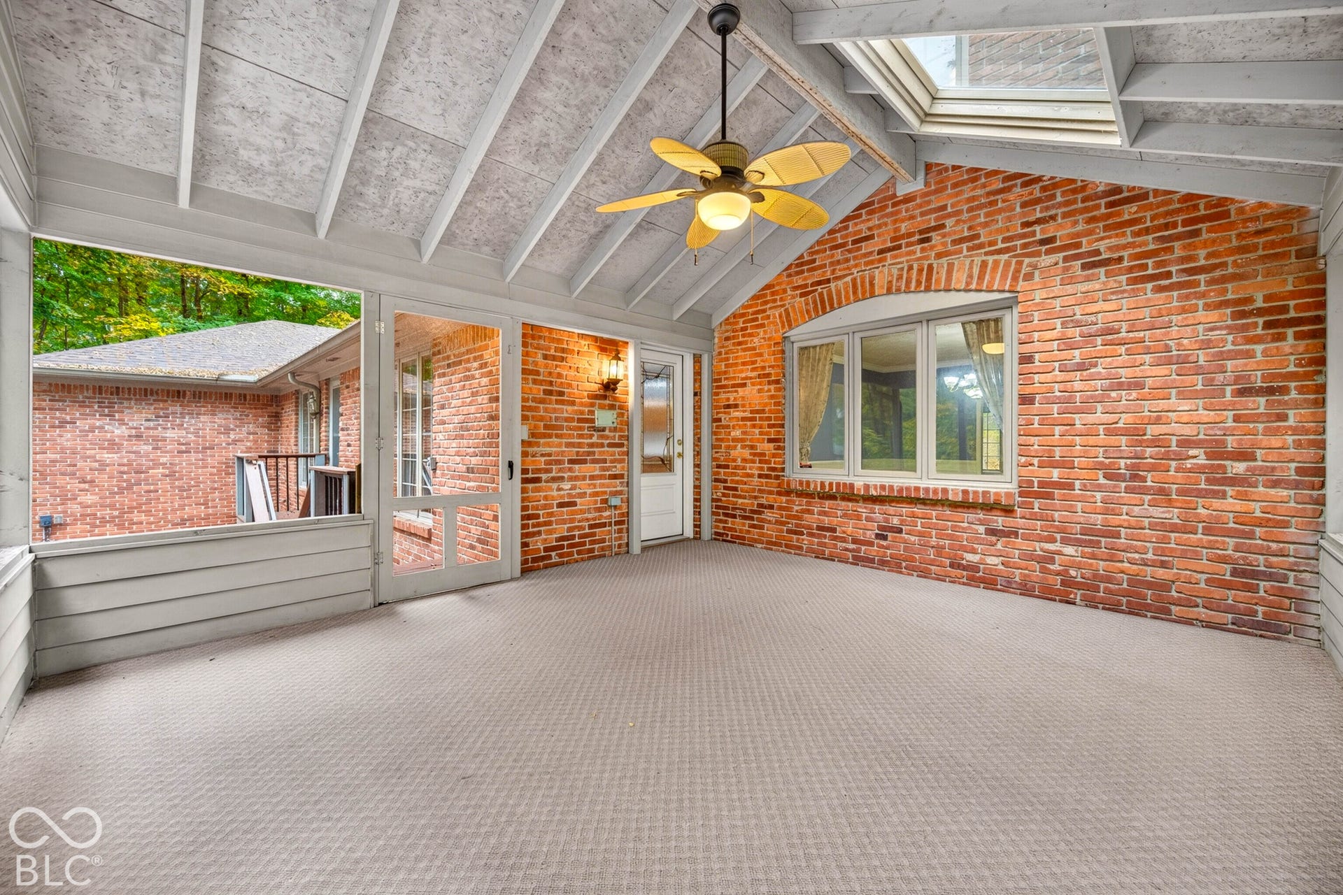 Screened porch featuring an exposed brick wall, vaulted ceiling with exposed rafters, skylight, and a ceiling fan