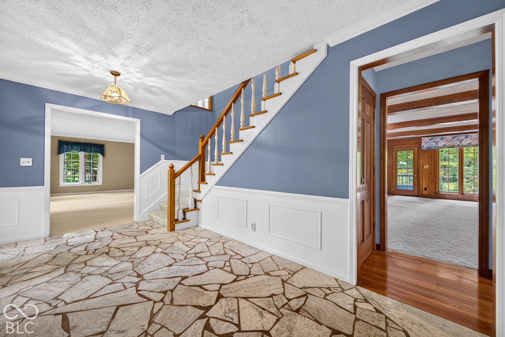 Foyer featuring flagstone flooring, wainscoting, and a staircase with a wooden handrail and turned balusters