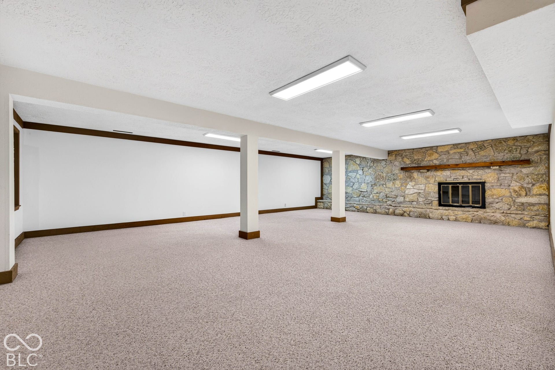 Spacious interior featuring a floor-to-ceiling stone fireplace, prominent wood mantel, neutral carpeting, and integrated overhead lighting