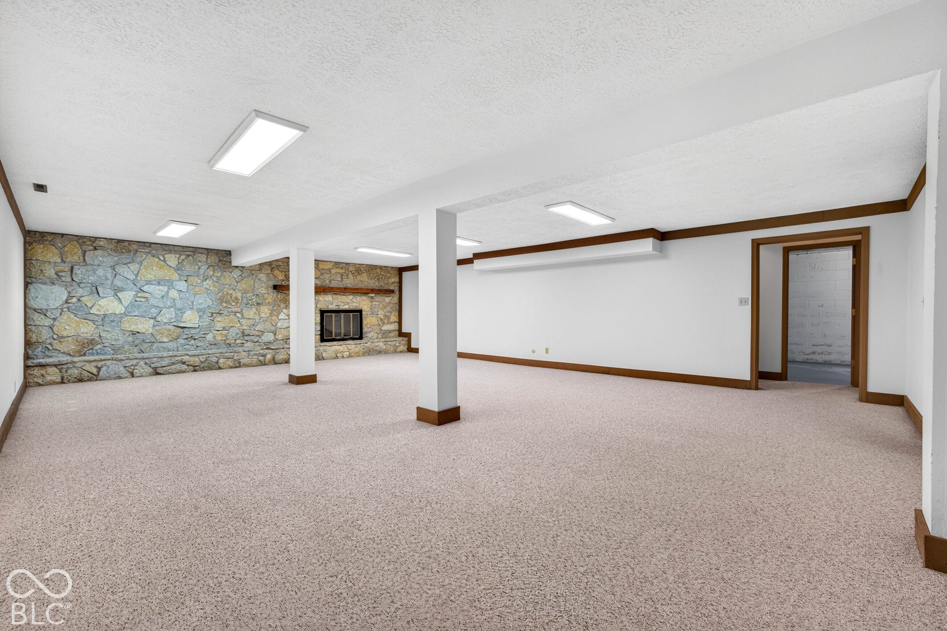 Expansive open-concept space featuring a floor-to-ceiling stone fireplace, built-in wooden mantel, recessed lighting, and neutral carpeting