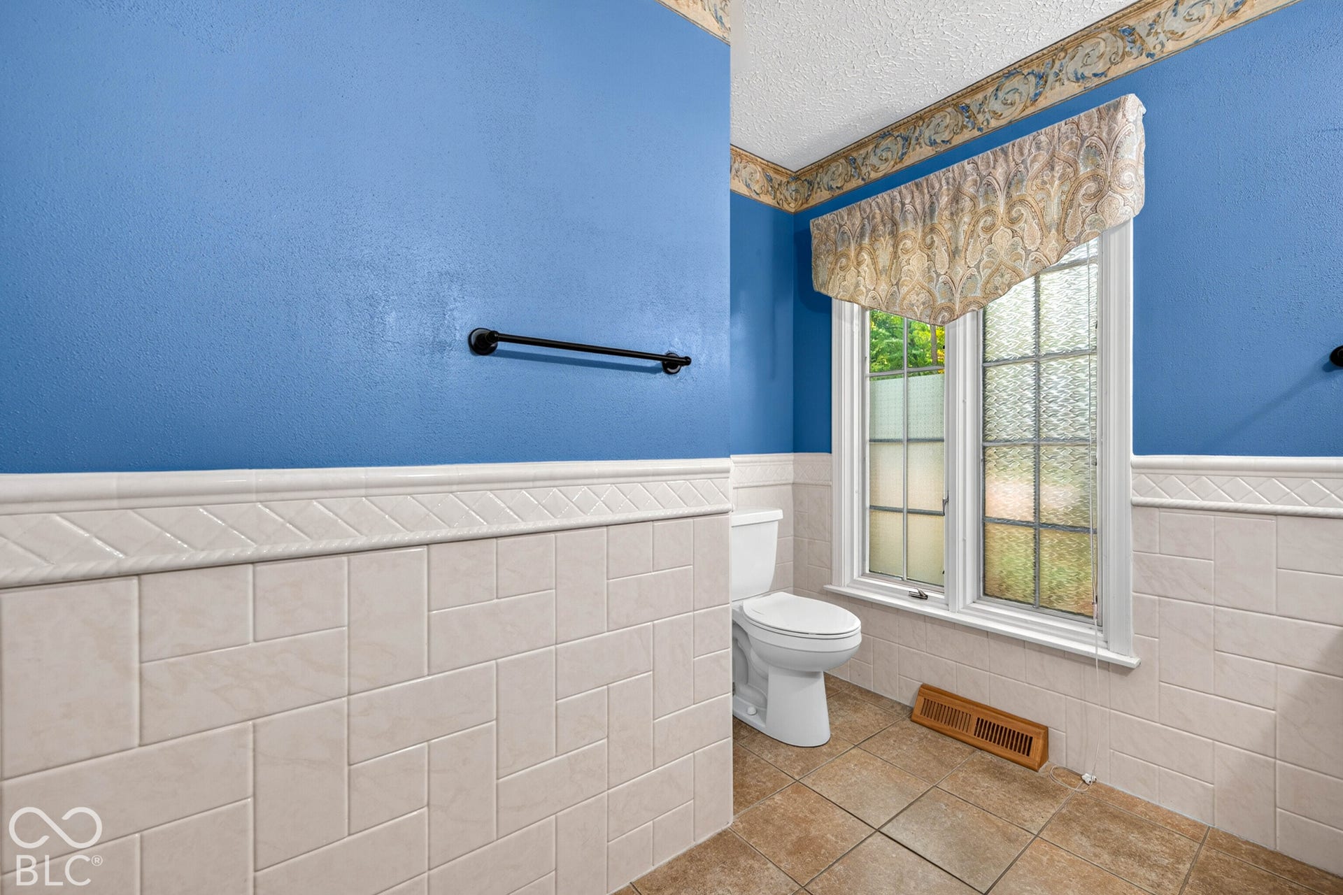 Bathroom featuring ceramic wall tiling with basketweave pattern inlay, neutral-toned floor tile, multi-pane window, and matte black hardware