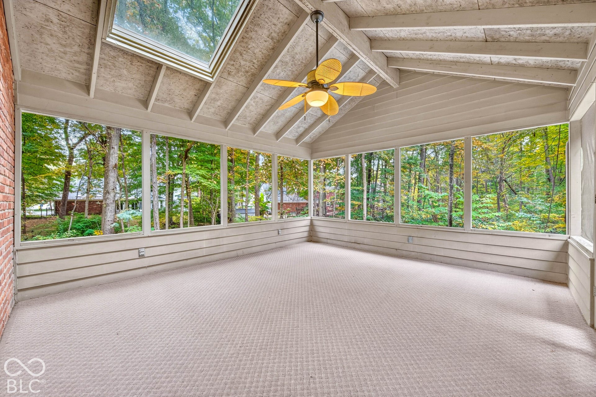 Screened porch featuring a vaulted ceiling with exposed beams, skylight, expansive wraparound windows, and a ceiling fan