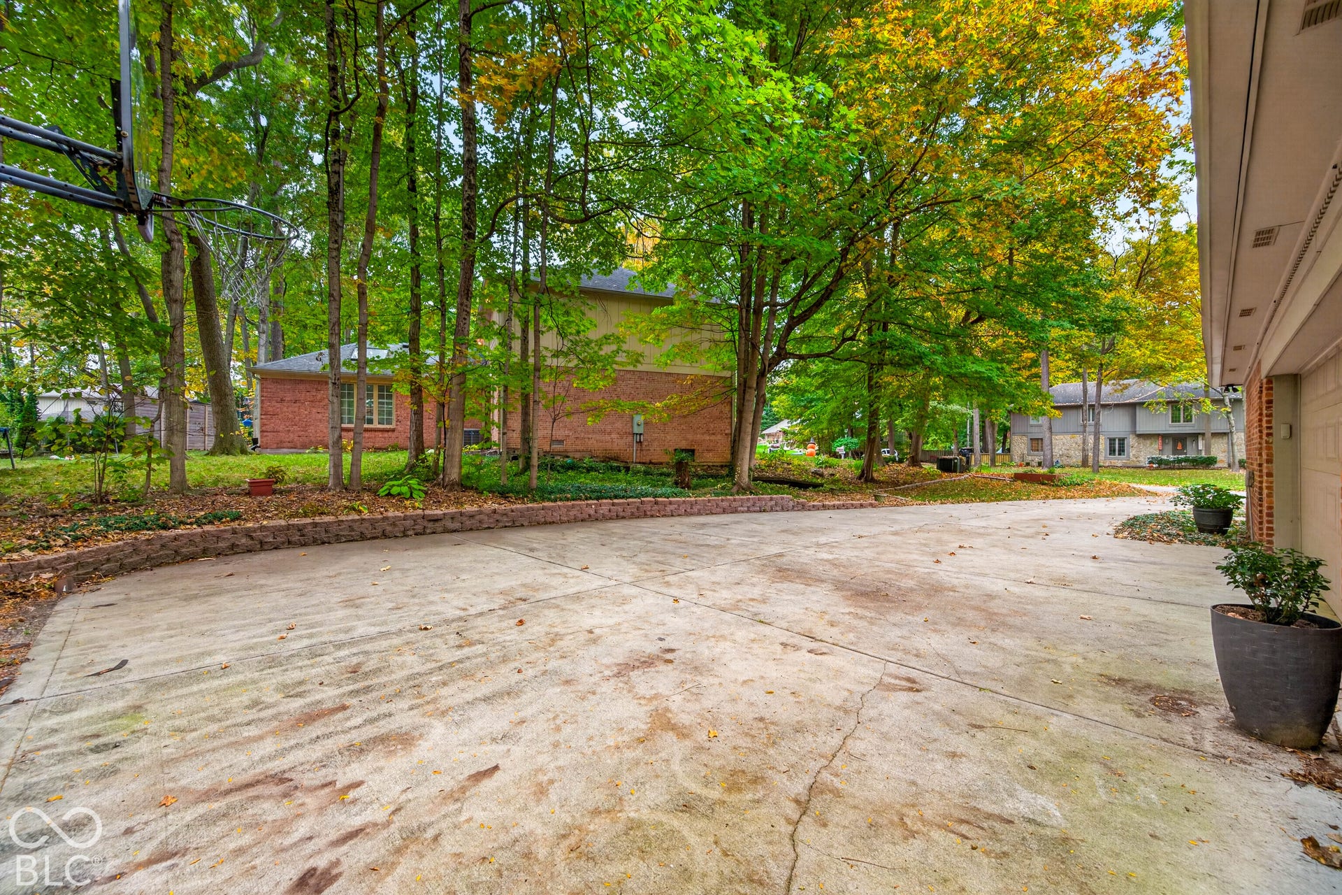 Spacious concrete driveway featuring a tiered masonry retaining wall and mature surrounding hardwood trees