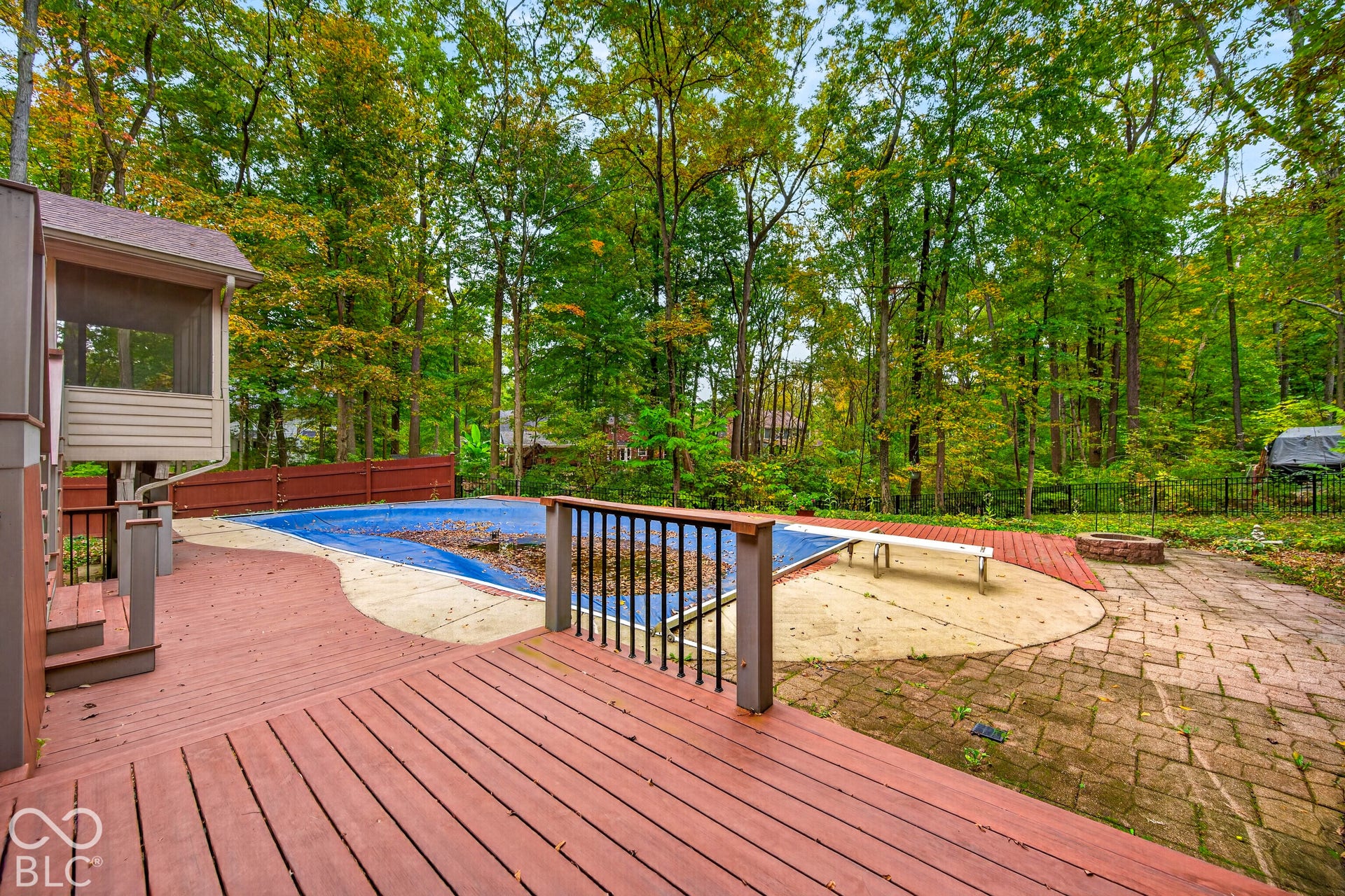Expansive outdoor living area featuring a wooden deck, a concrete pool surround, an in-ground swimming pool, a brick fire pit, and a screened-in porch