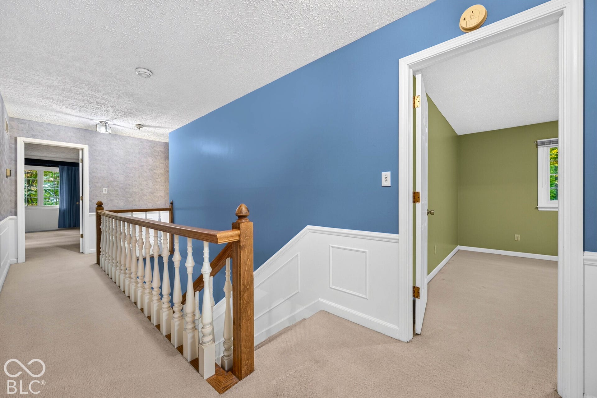 Staircase featuring wood handrails, decorative spindle balusters, and white wainscoting paneling