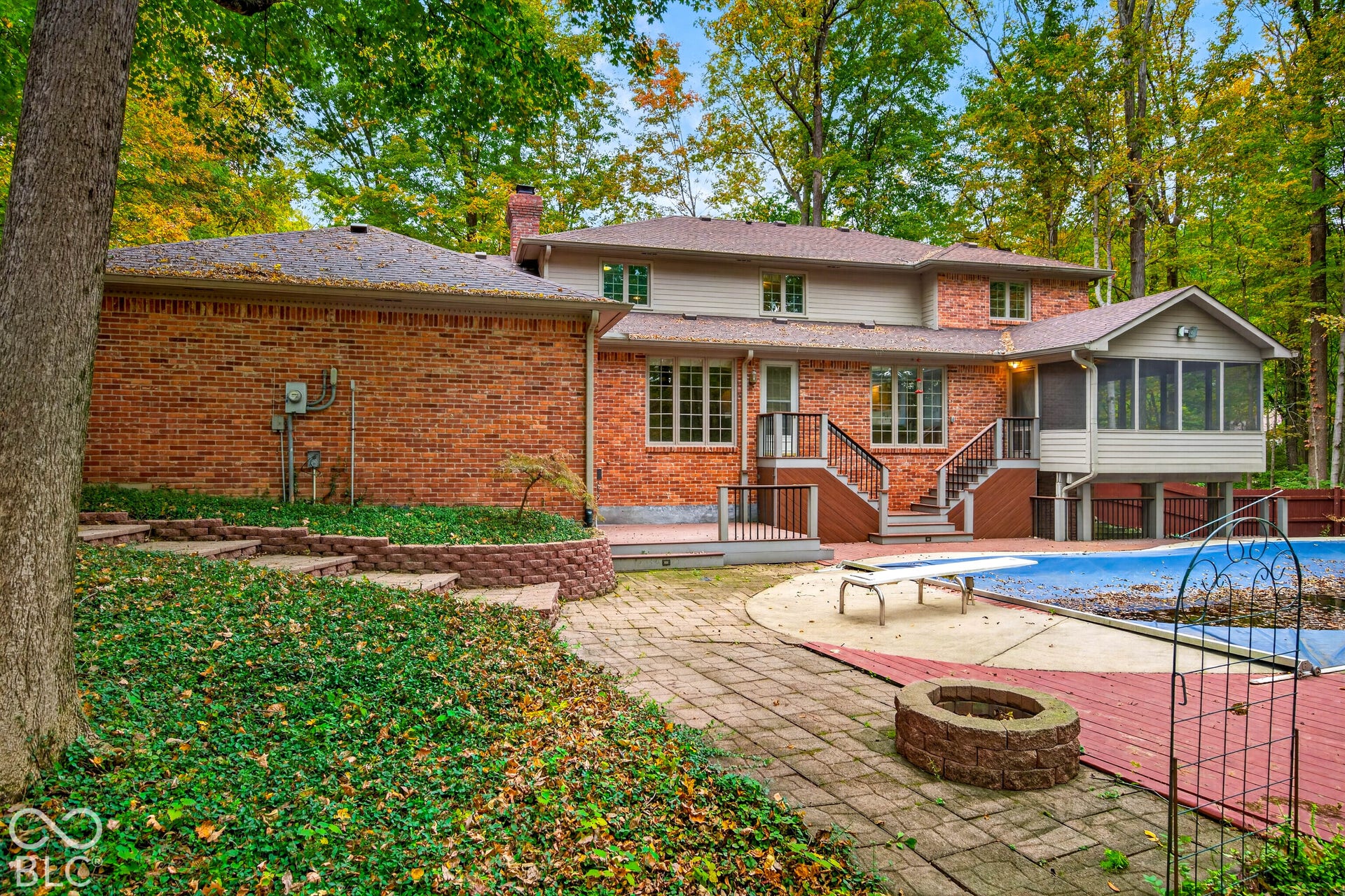 Brick exterior residence featuring a tiered landscape, stone-paver patio, in-ground pool, and a screened-in porch with elevated staircase