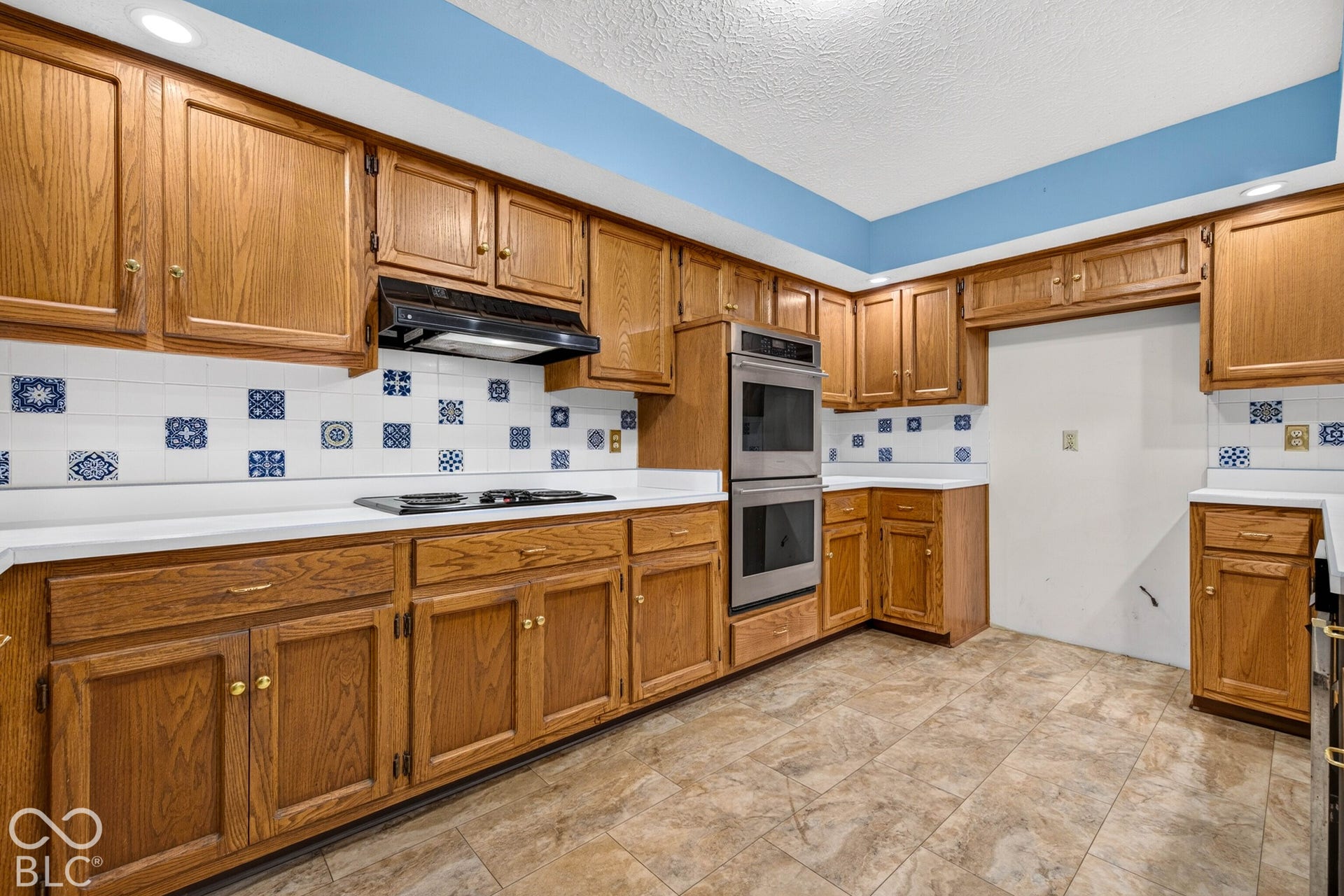 Kitchen featuring oak-finish cabinetry, built-in stainless steel double wall ovens, a black cooktop, decorative tile backsplash, and solid surface countertops