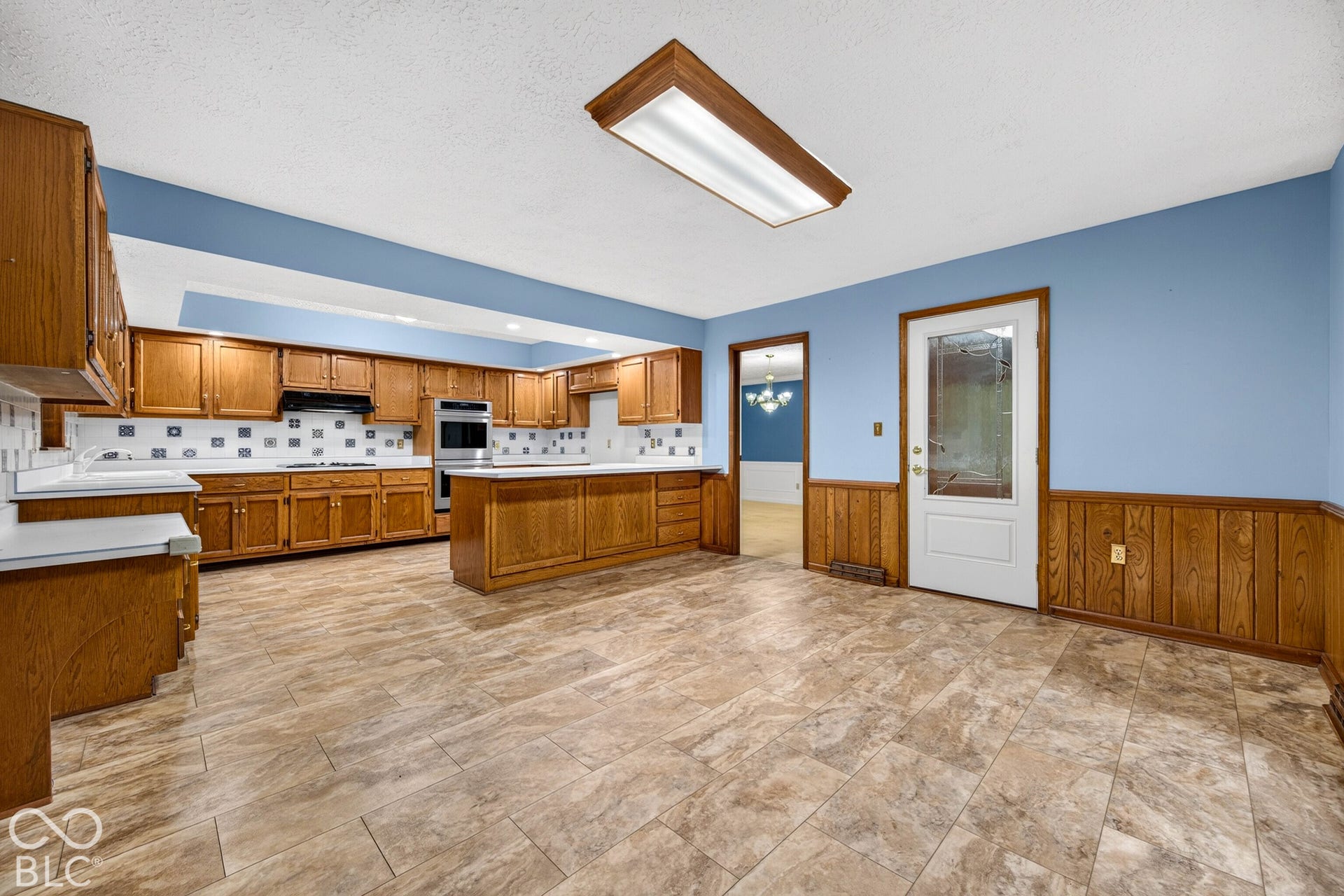 Kitchen featuring wood cabinetry, integrated double wall ovens, ceramic tile flooring, and half-height wood wainscoting