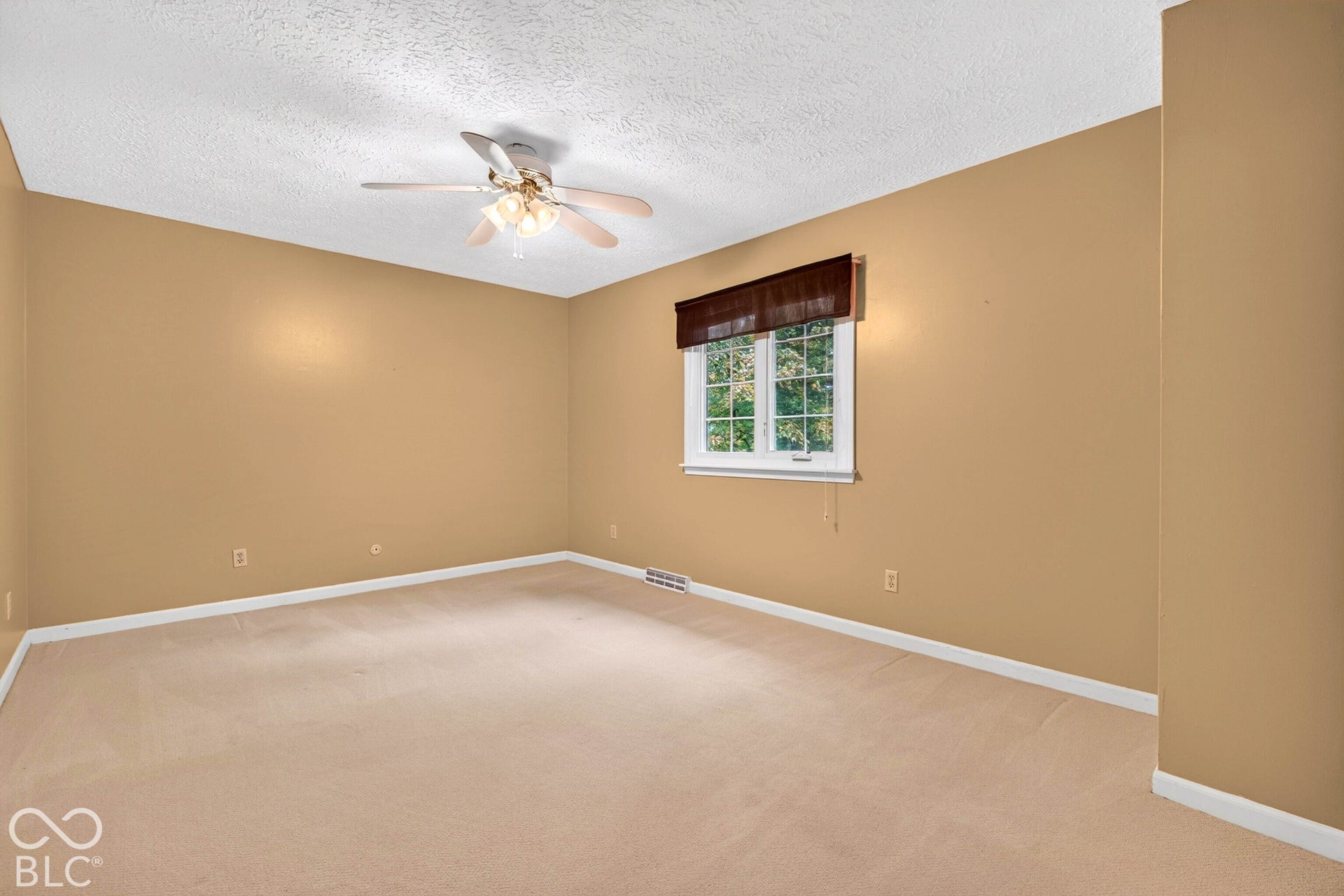 Interior space featuring neutral wall tones, wall-to-wall carpeting, a multi-blade ceiling fan with integrated light fixture, and a window with a valance