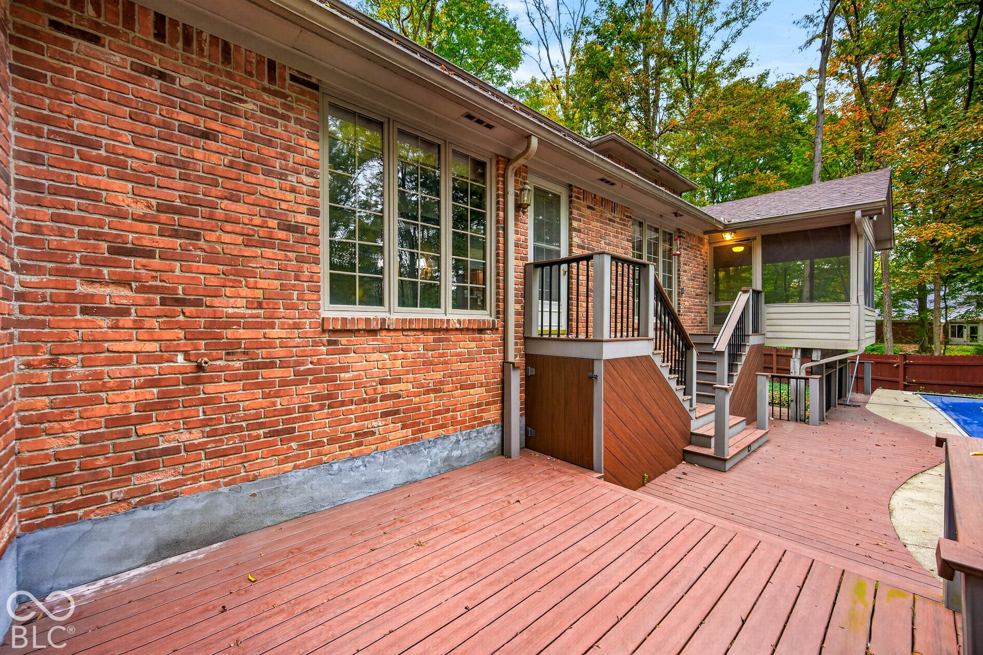 Exterior brick facade featuring a multi-level composite deck, screened-in porch, and outdoor pool