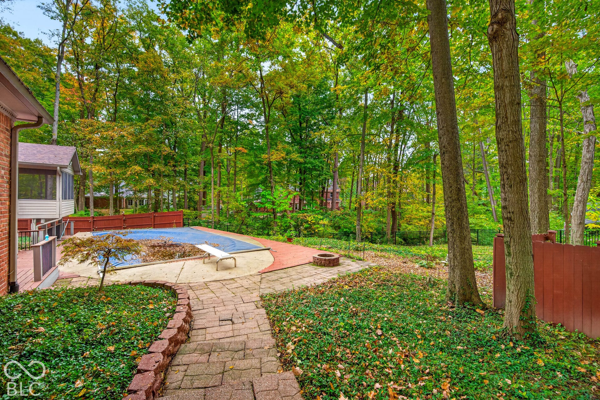 Rear yard featuring a paved stone patio, in-ground pool with a diving board, stone fire pit, and mature tree canopy