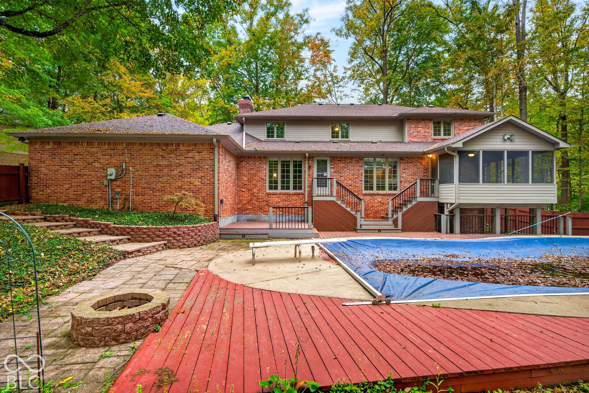 Exterior featuring a multi-level red brick facade, a screened porch, a multi-tiered wooden deck, an in-ground swimming pool, and a stone-paver fire pit