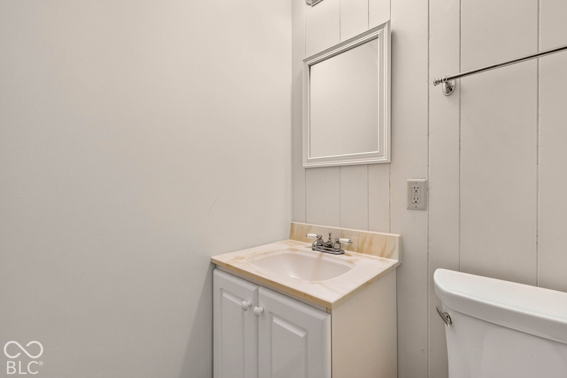 Wall-mounted mirror, vertical wood-paneling accent wall, white vanity cabinet with stone-finish countertop, integrated sink, and chrome-finish hardware