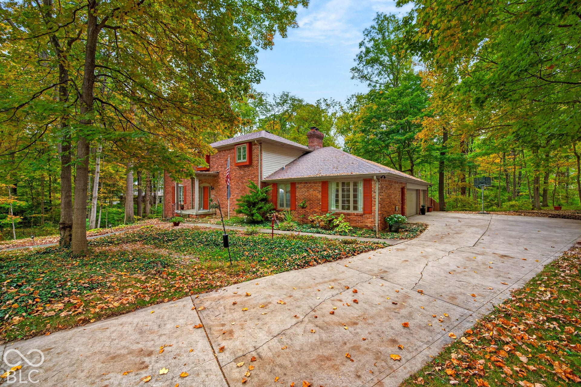 Brick exterior featuring multi-pane windows, louvered shutters, a chimney, and a concrete driveway