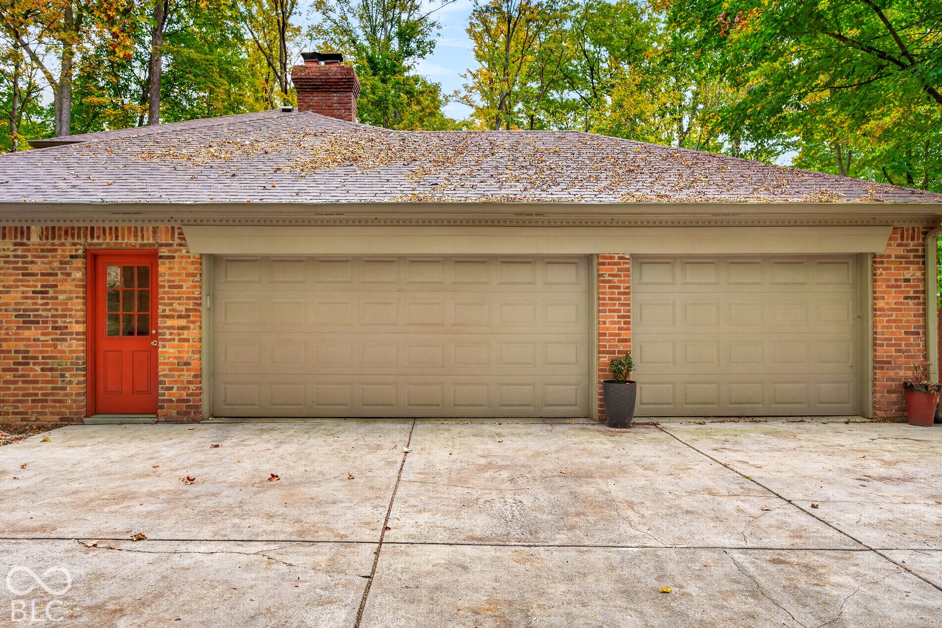 Exterior featuring red brick masonry, a dual-bay garage, a separate single-panel entry door with windowed accents, a brick chimney, and a concrete driveway