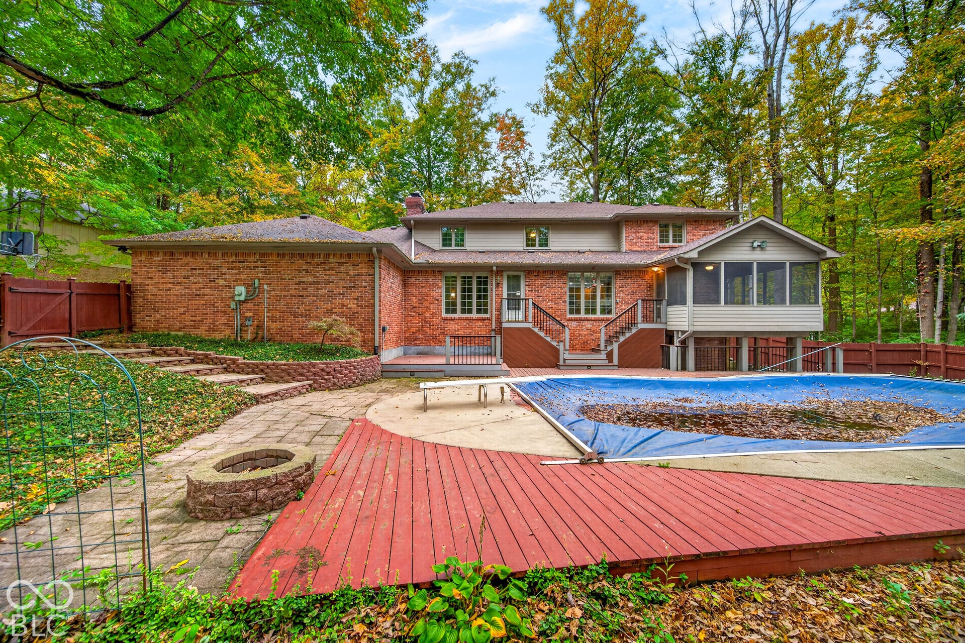 Brick exterior residence featuring a screened-in porch, multi-level wood decking, integrated paver patio with stone fire pit, and in-ground pool