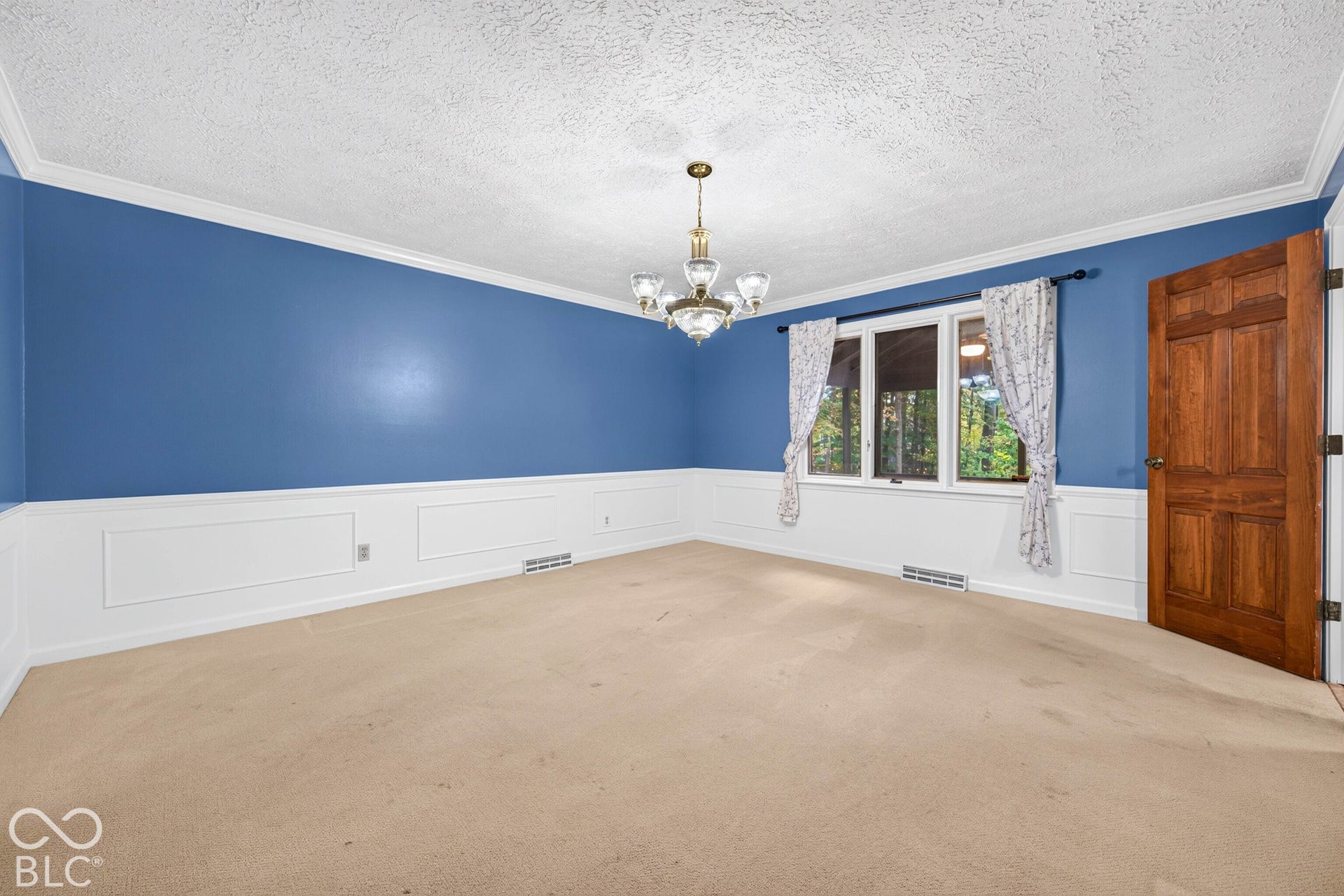Room featuring white wainscoting, a multi-arm chandelier, and a solid wood six-panel door