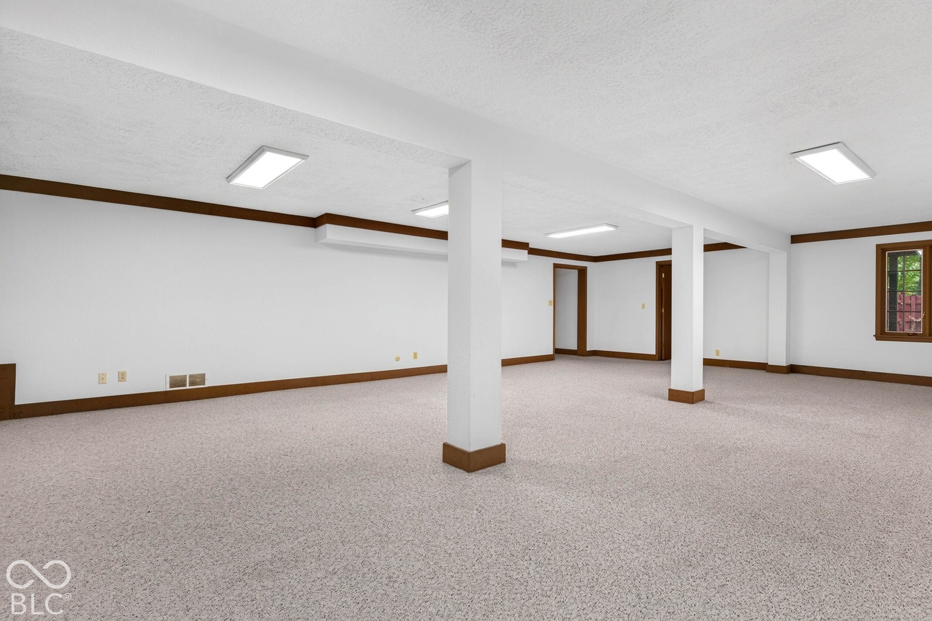 Open-concept interior space featuring neutral carpeting, white walls with dark-finish crown molding, structural support columns, and recessed lighting fixtures