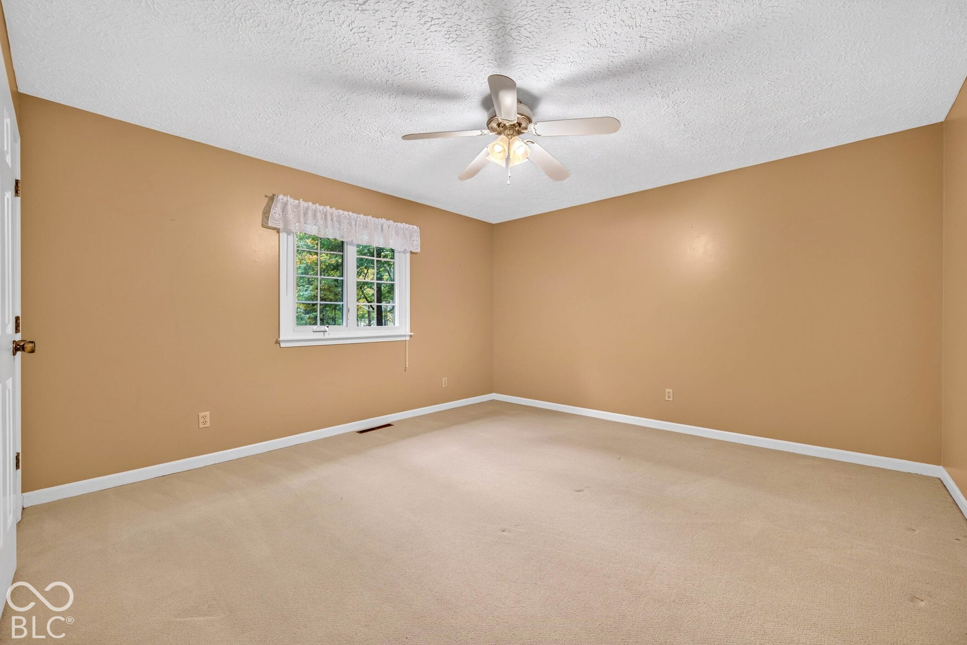 Room interior featuring neutral wall paint, wall-to-wall carpeting, multi-pane window, and a ceiling-mounted light fixture with a multi-blade fan
