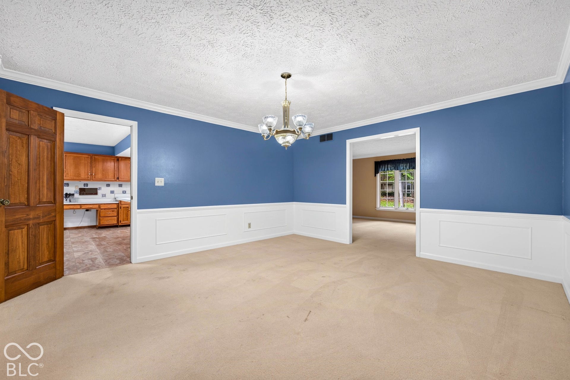 Interior room featuring white wainscoting, a multi-arm metallic chandelier, a solid wood six-panel door, and crown molding
