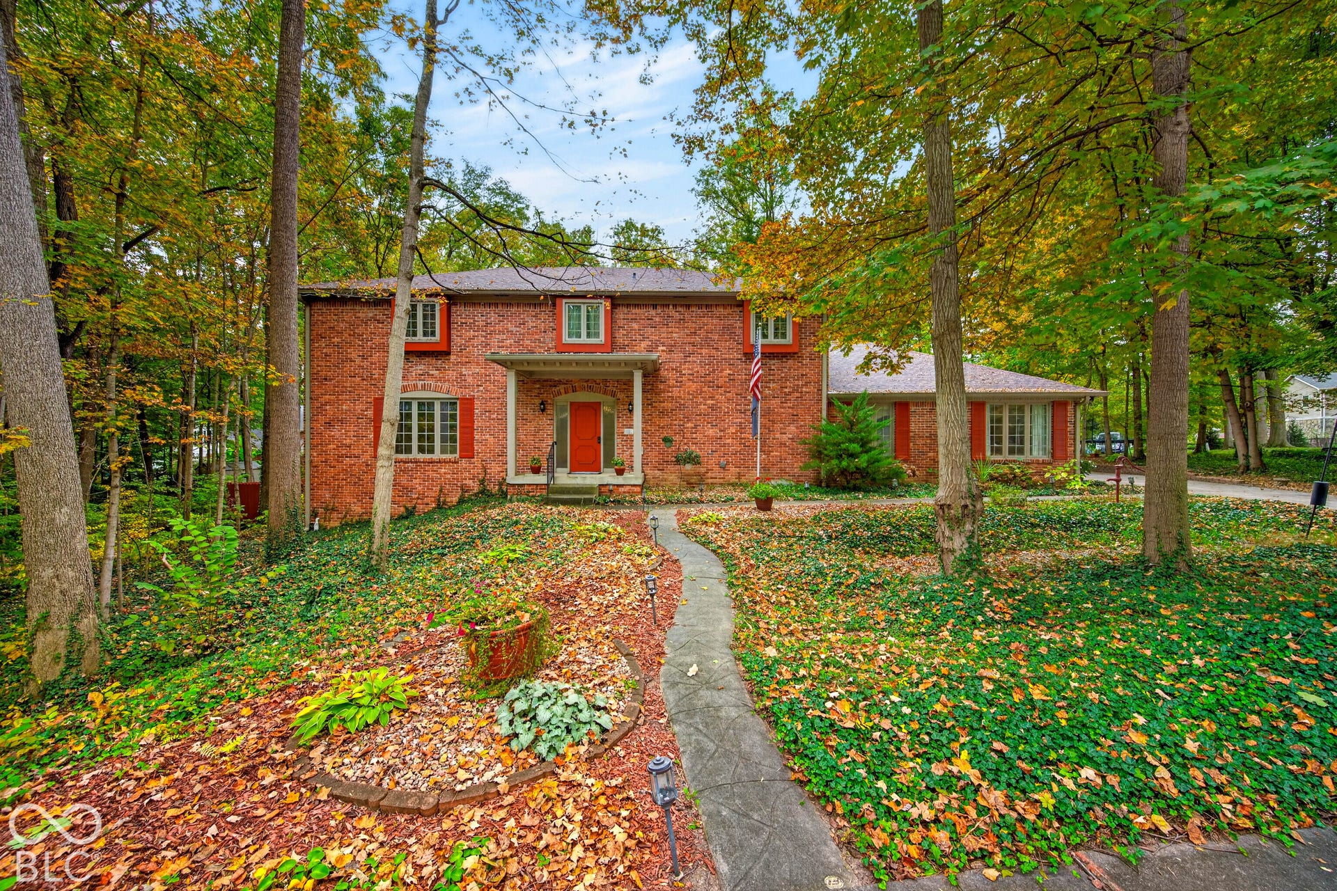 Two-story brick exterior featuring a covered front entry, multi-pane windows, decorative shutters, and mature trees