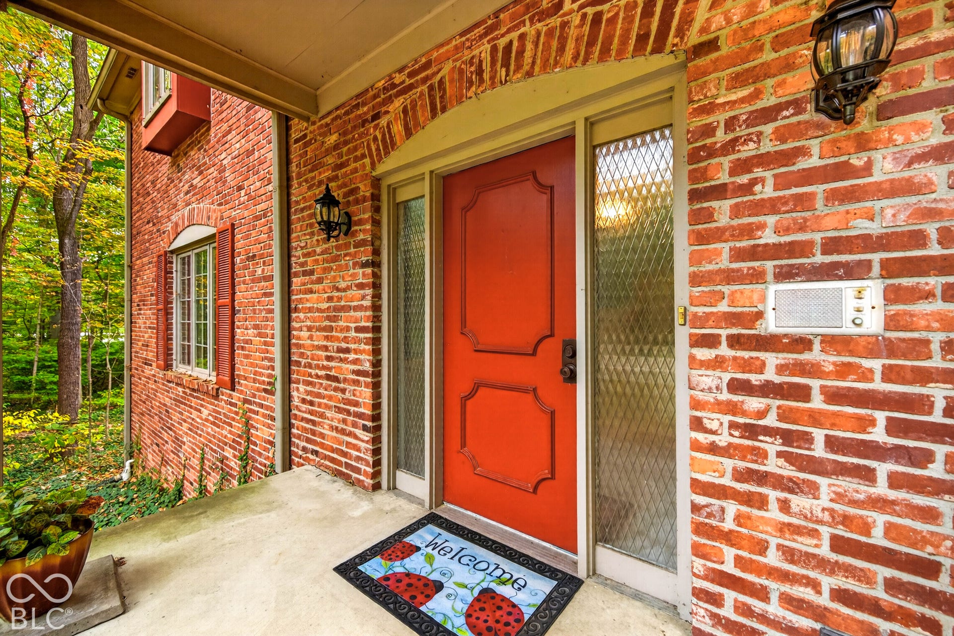 Covered front porch featuring a red entry door with decorative molding, full-length sidelights with wire-mesh glass, and exterior brick masonry