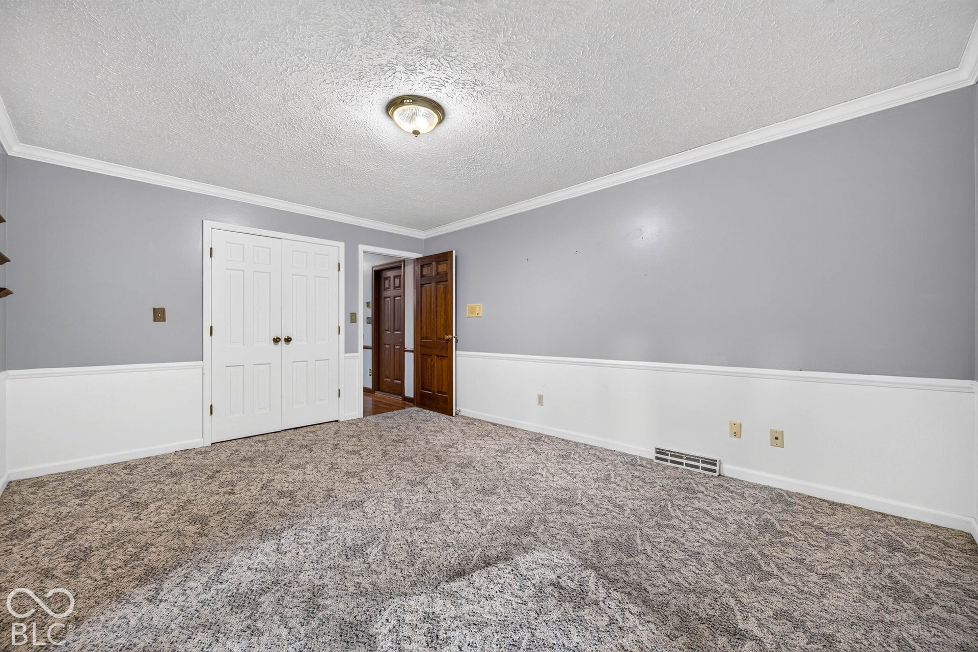 Interior room featuring dual-tone wall paint with wainscoting, textured ceiling, flush-mount lighting, carpeted flooring, and a six-panel wood door
