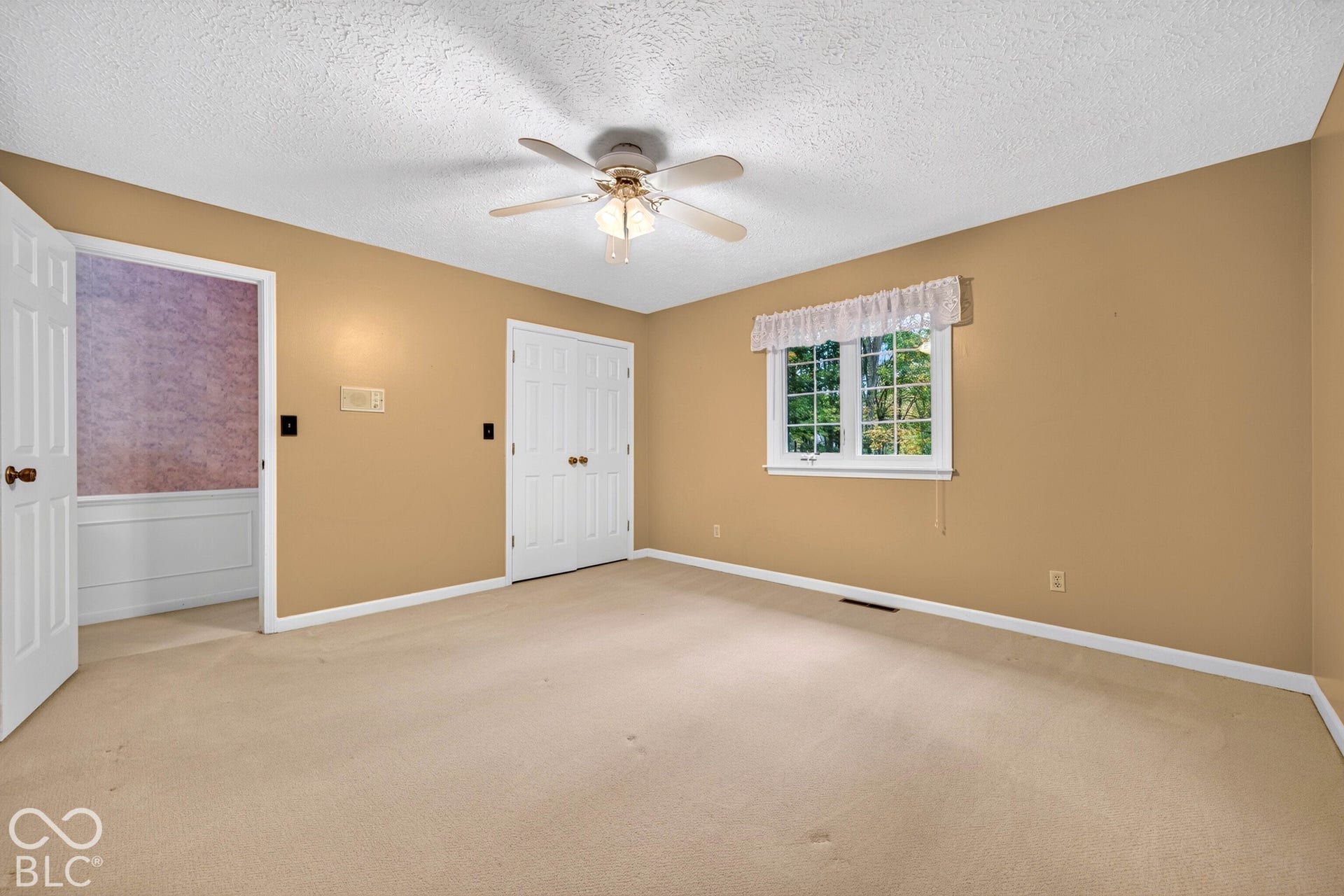Room featuring neutral carpeting, double-door closet, multi-pane window with valance, and a ceiling fan with light fixture