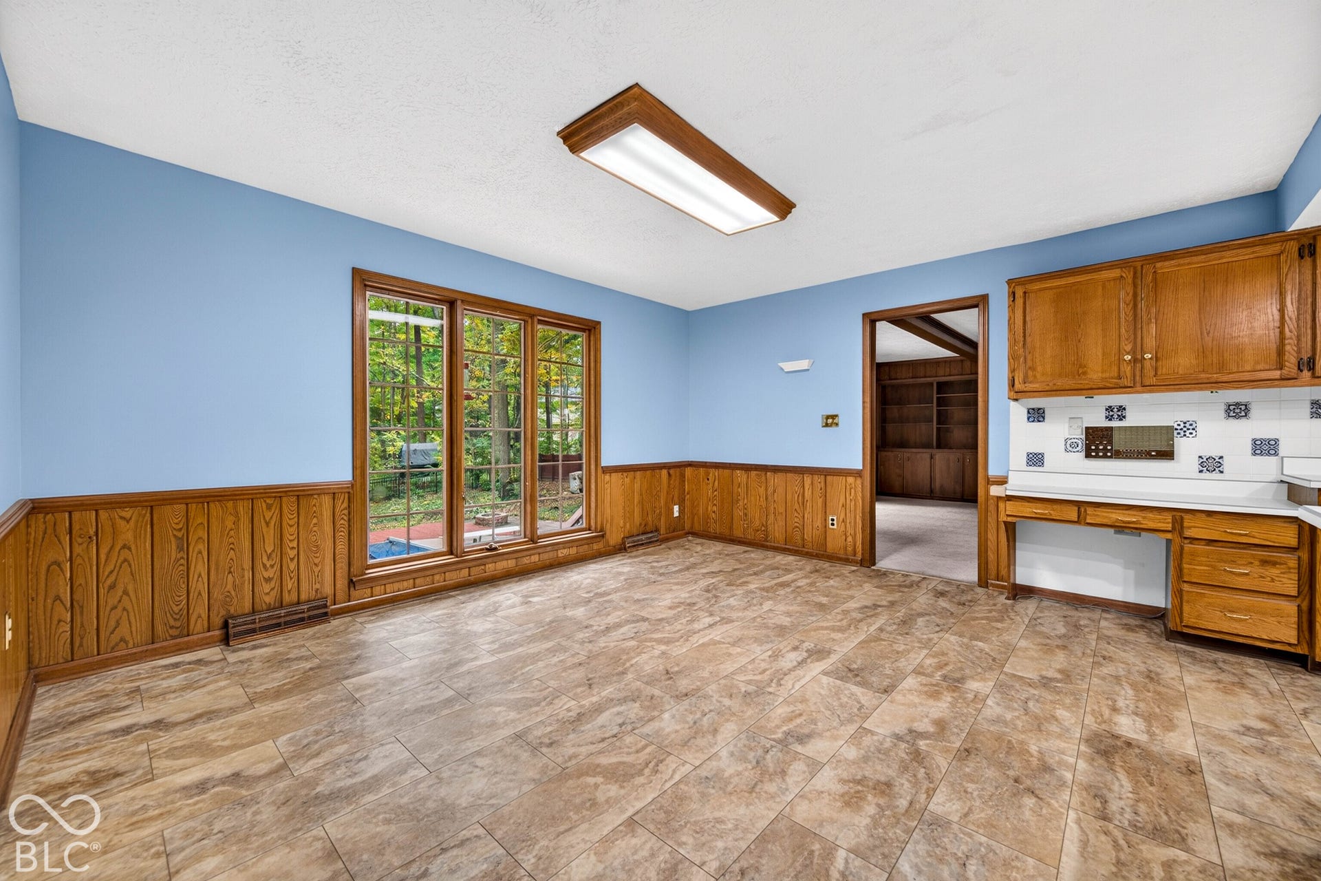 Wood-paneled wainscoting, ceramic tile flooring, built-in wooden cabinetry, recessed desk area, and oversized multi-pane window