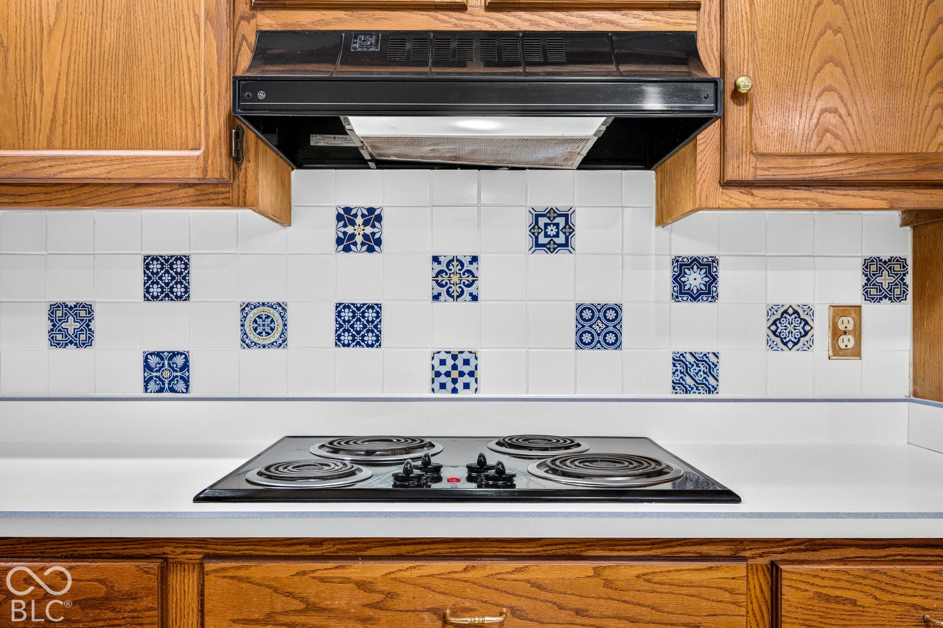 Kitchen featuring wood cabinetry, a four-burner electric cooktop, a black range hood, and a decorative tile backsplash