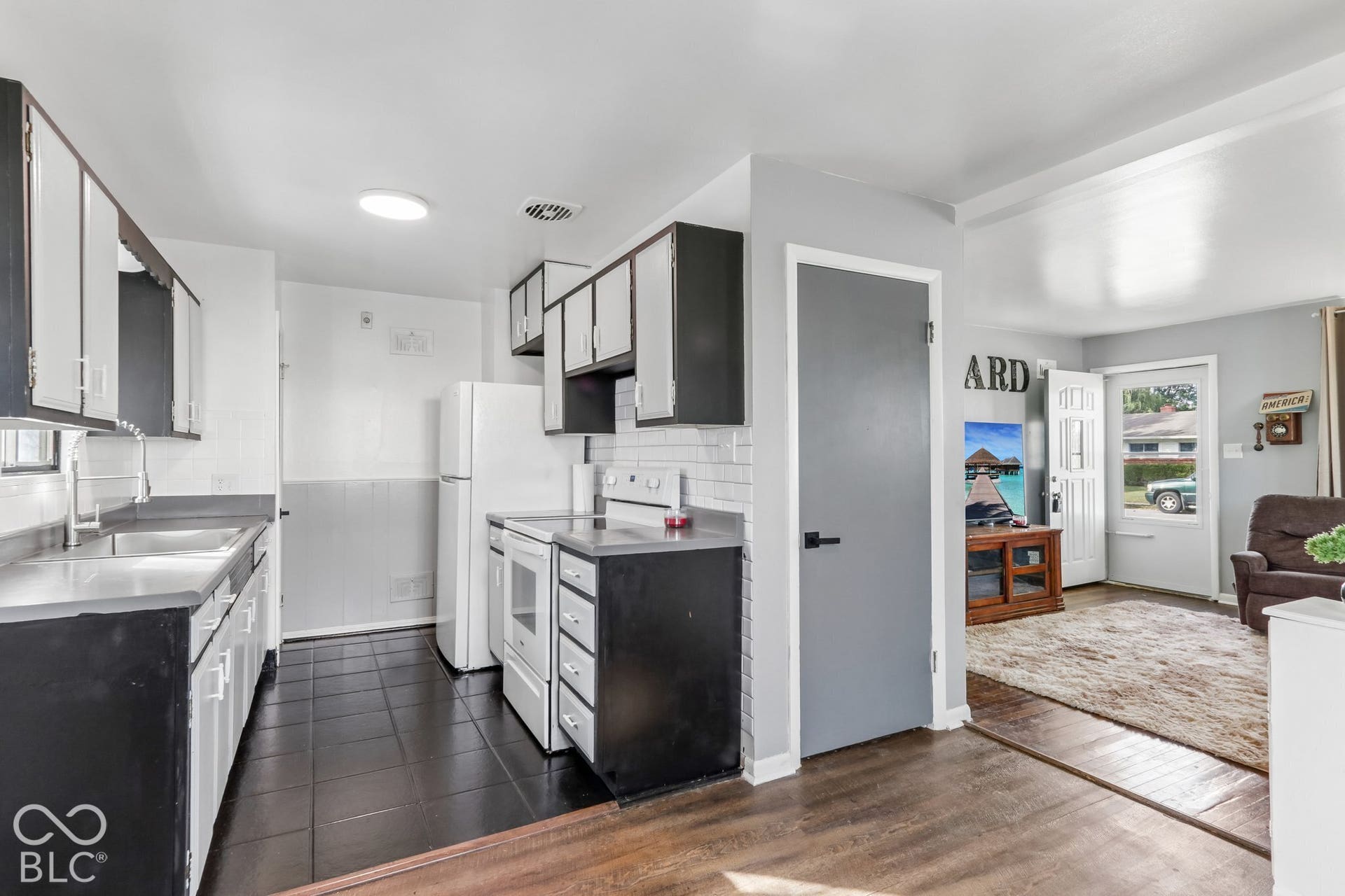 Kitchen featuring dark-toned cabinetry, white tile backsplash, dark tile flooring, and integrated white appliances