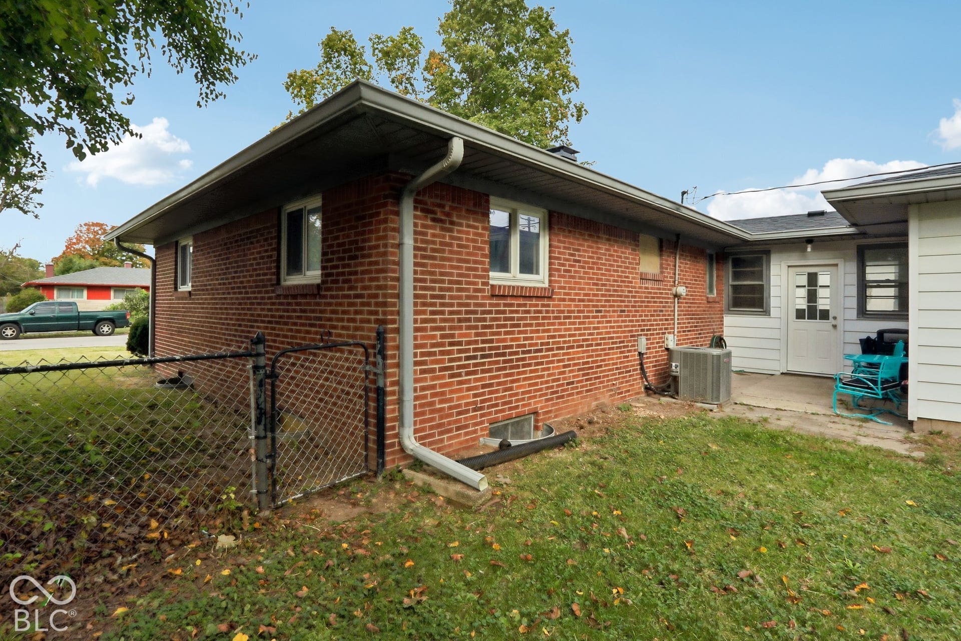 Exterior featuring red brick masonry, white siding, concrete patio, and chain-link perimeter fencing