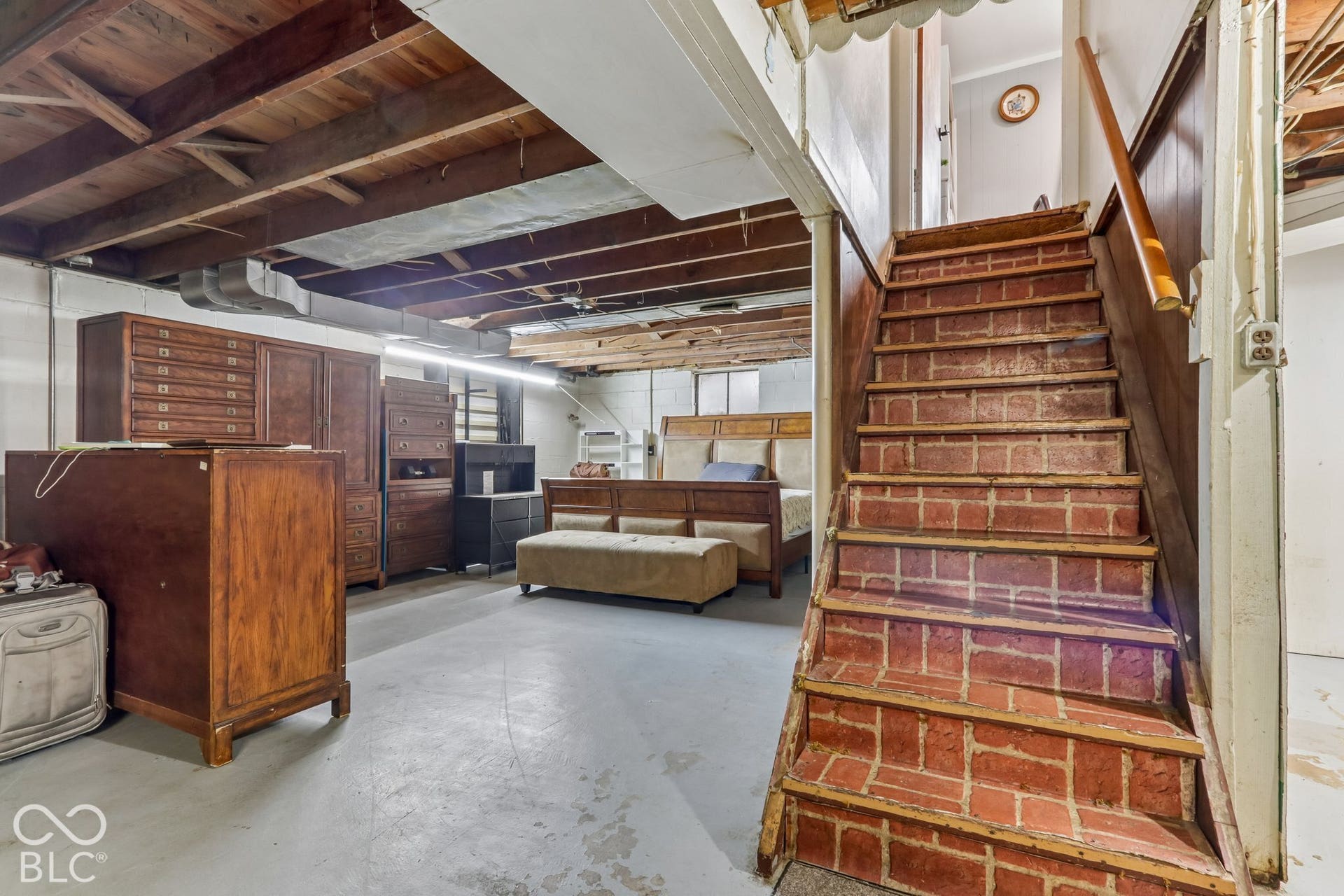 Exposed wood ceiling joists, staircase with brick-finish treads, painted concrete flooring, and wood-finish wall paneling