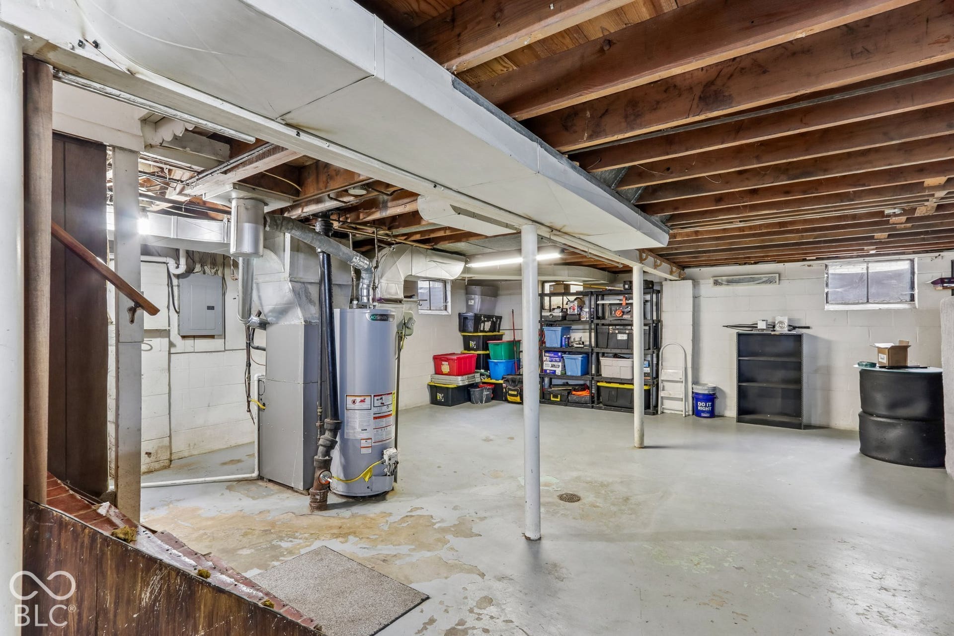 Unfinished basement featuring exposed wood ceiling joists, painted masonry walls, painted concrete flooring, and metal support columns