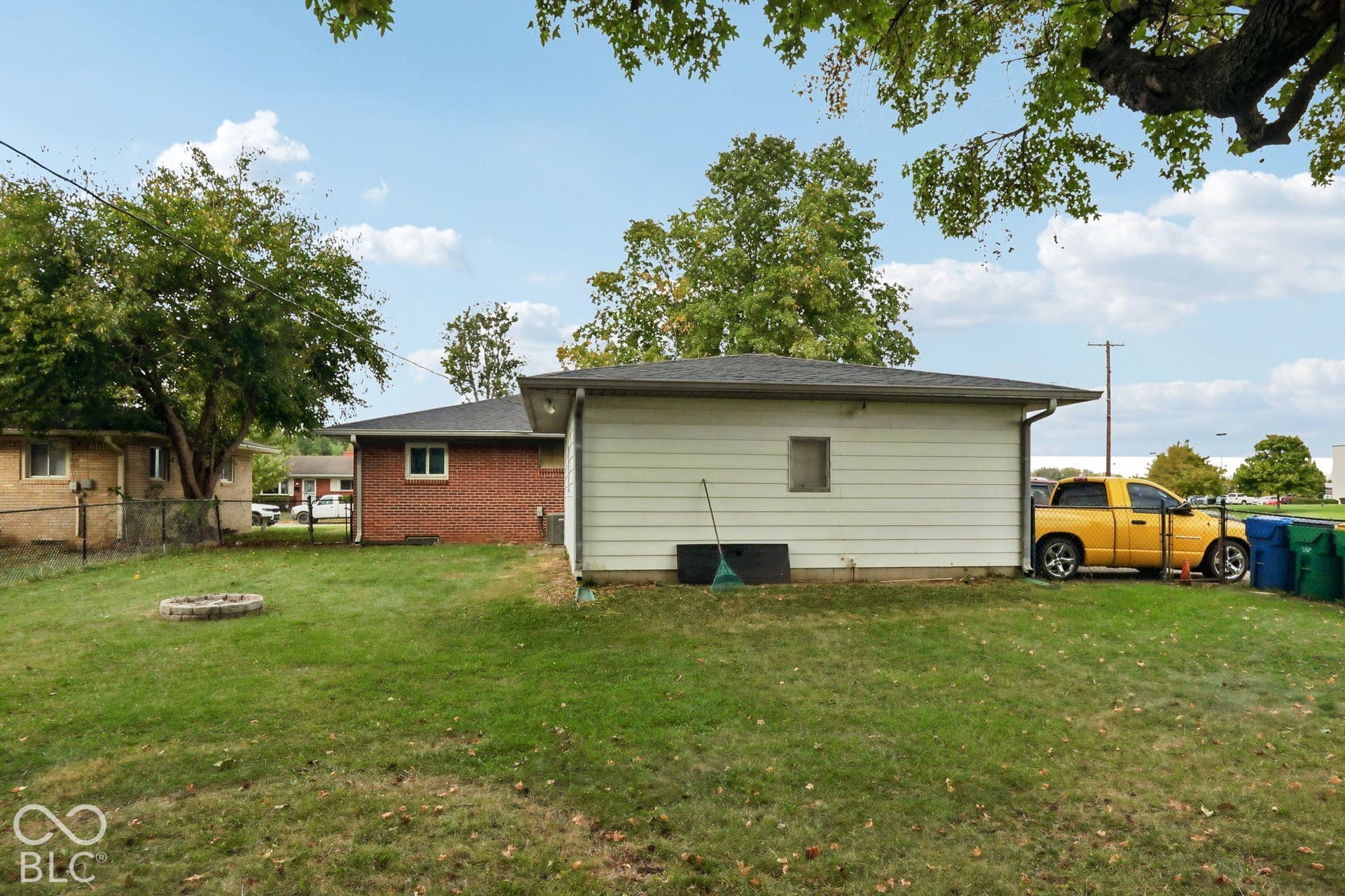 Backyard featuring a masonry exterior, detached garage, stone-perimeter fire pit, chain-link fencing, and mature trees