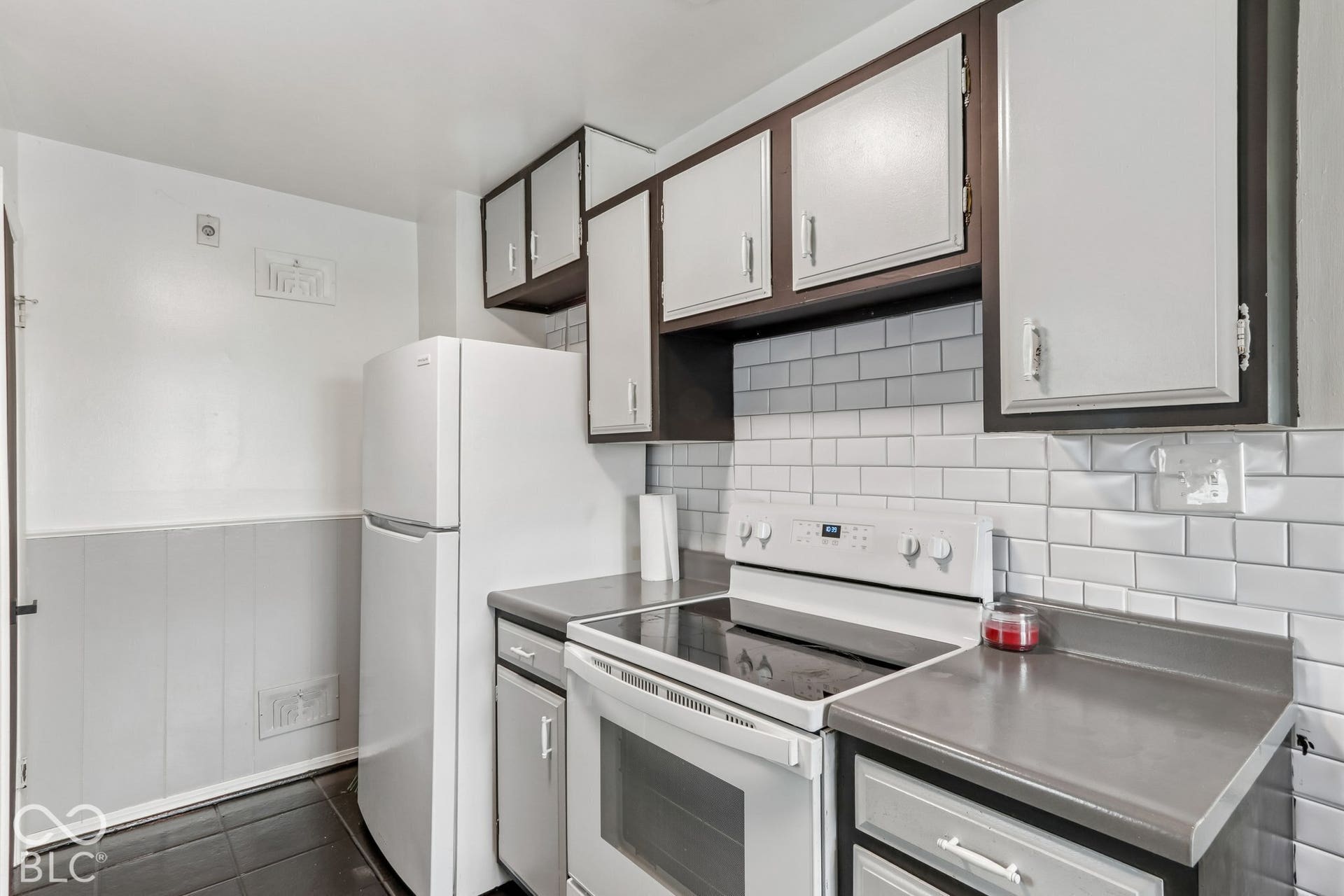 Kitchen featuring white subway tile backsplash, solid-surface countertops, two-toned cabinetry, and white appliances
