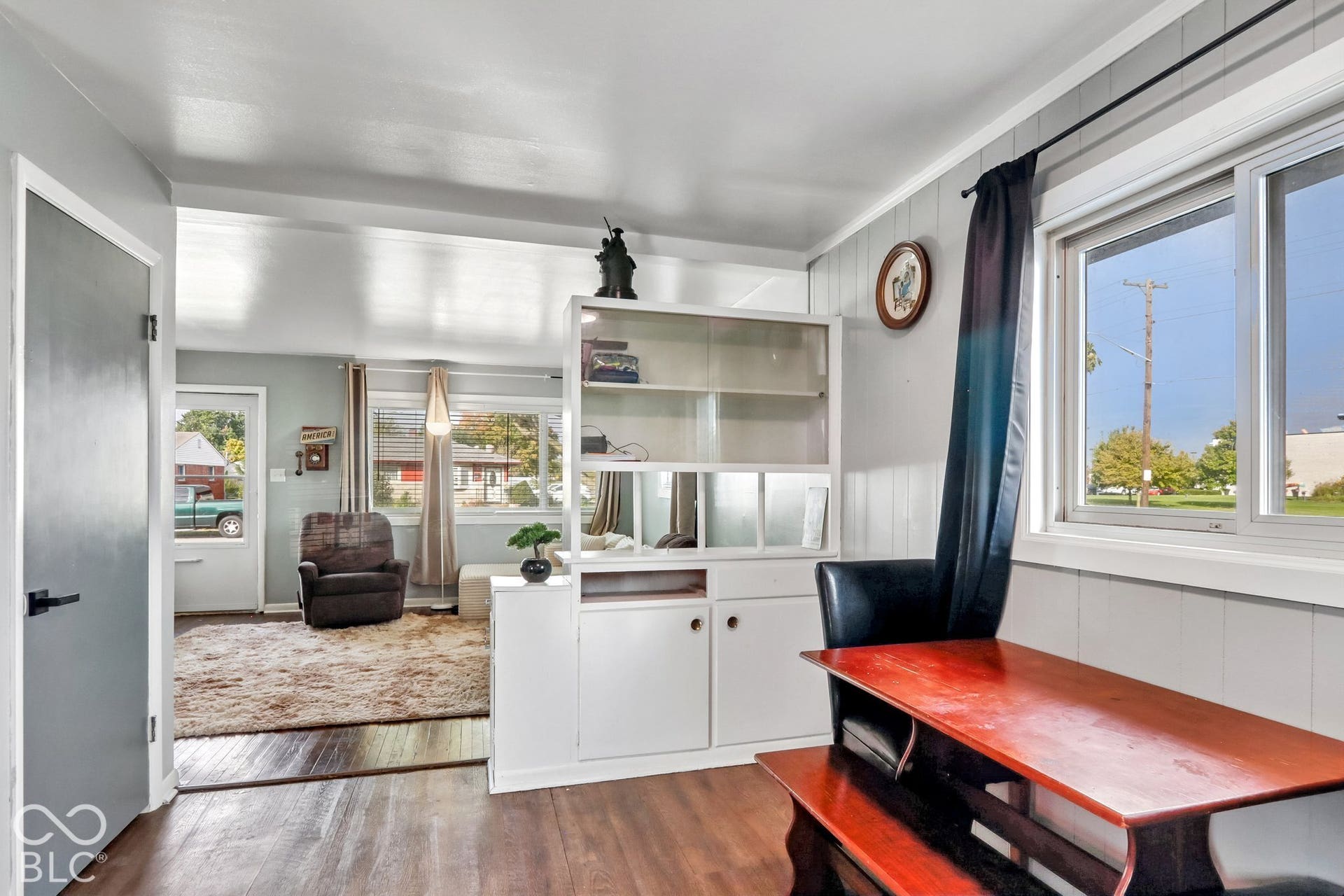Living area featuring wood-finish flooring, white built-in shelving, and large windows with natural light