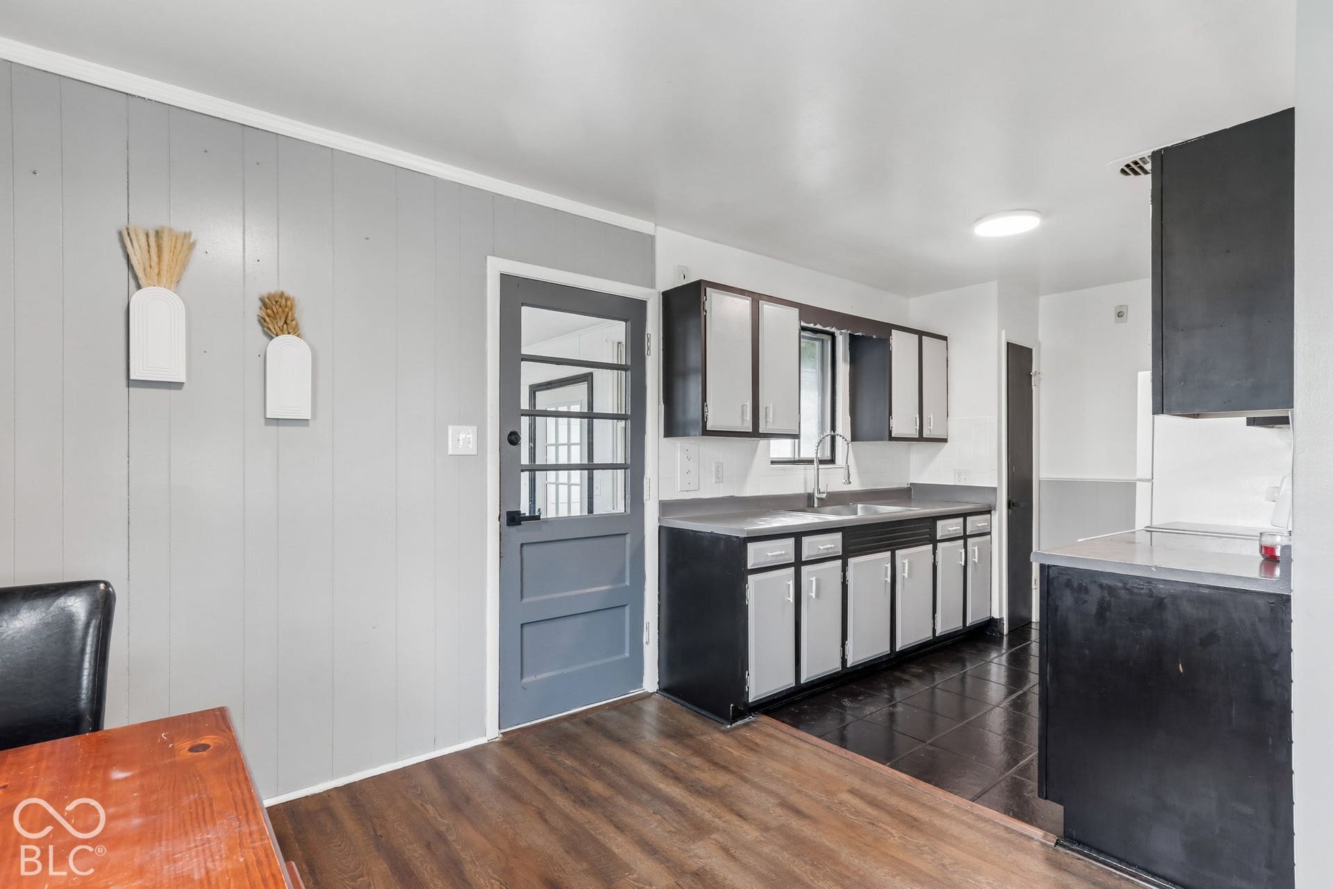 Kitchen featuring two-tone cabinetry, solid surface countertops, a stainless steel faucet, wood-finish flooring, and a glass-paneled exterior door