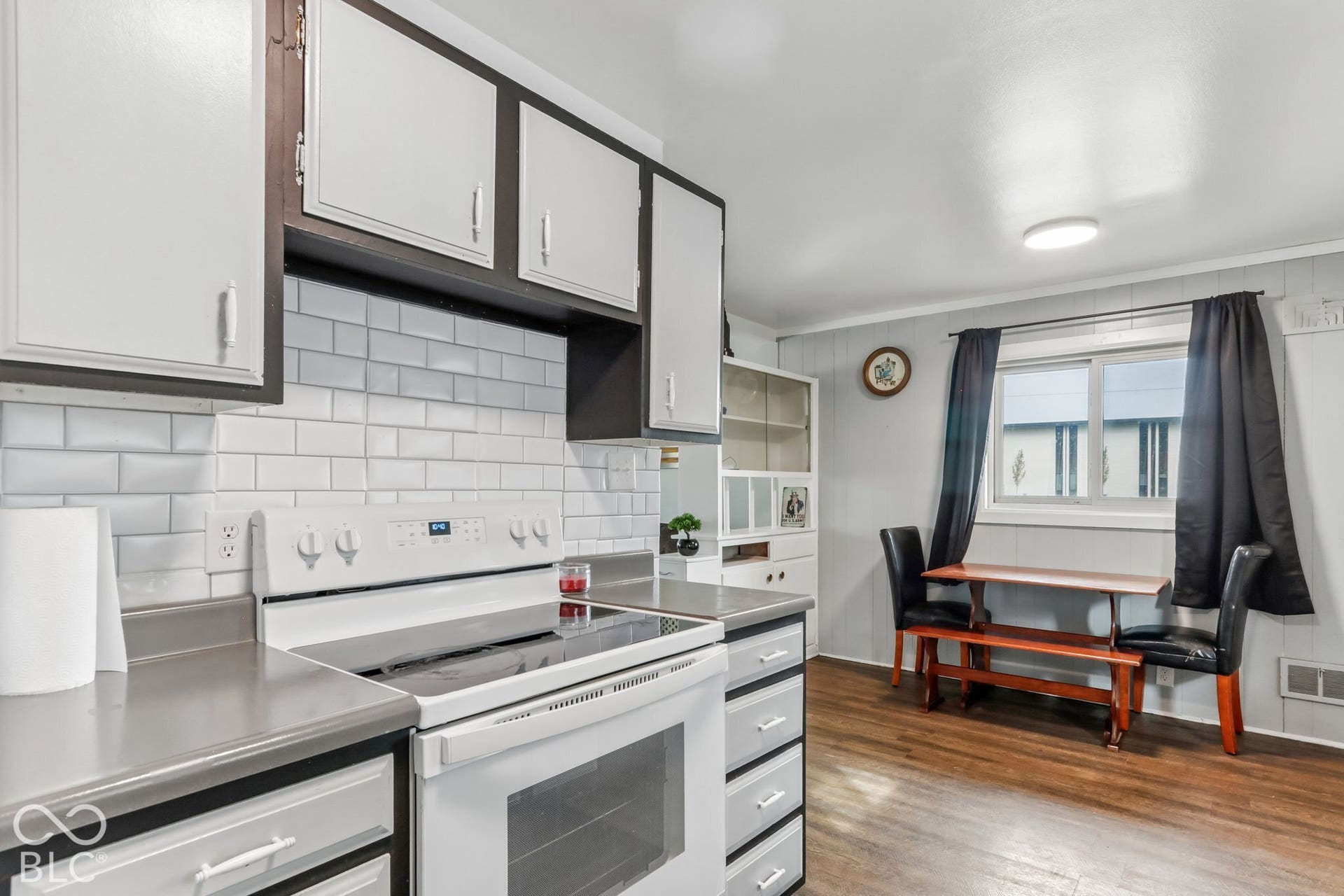 Kitchen featuring white cabinetry with contrasting trim, white subway tile backsplash, solid-surface countertops, built-in shelving, and wood-finish flooring