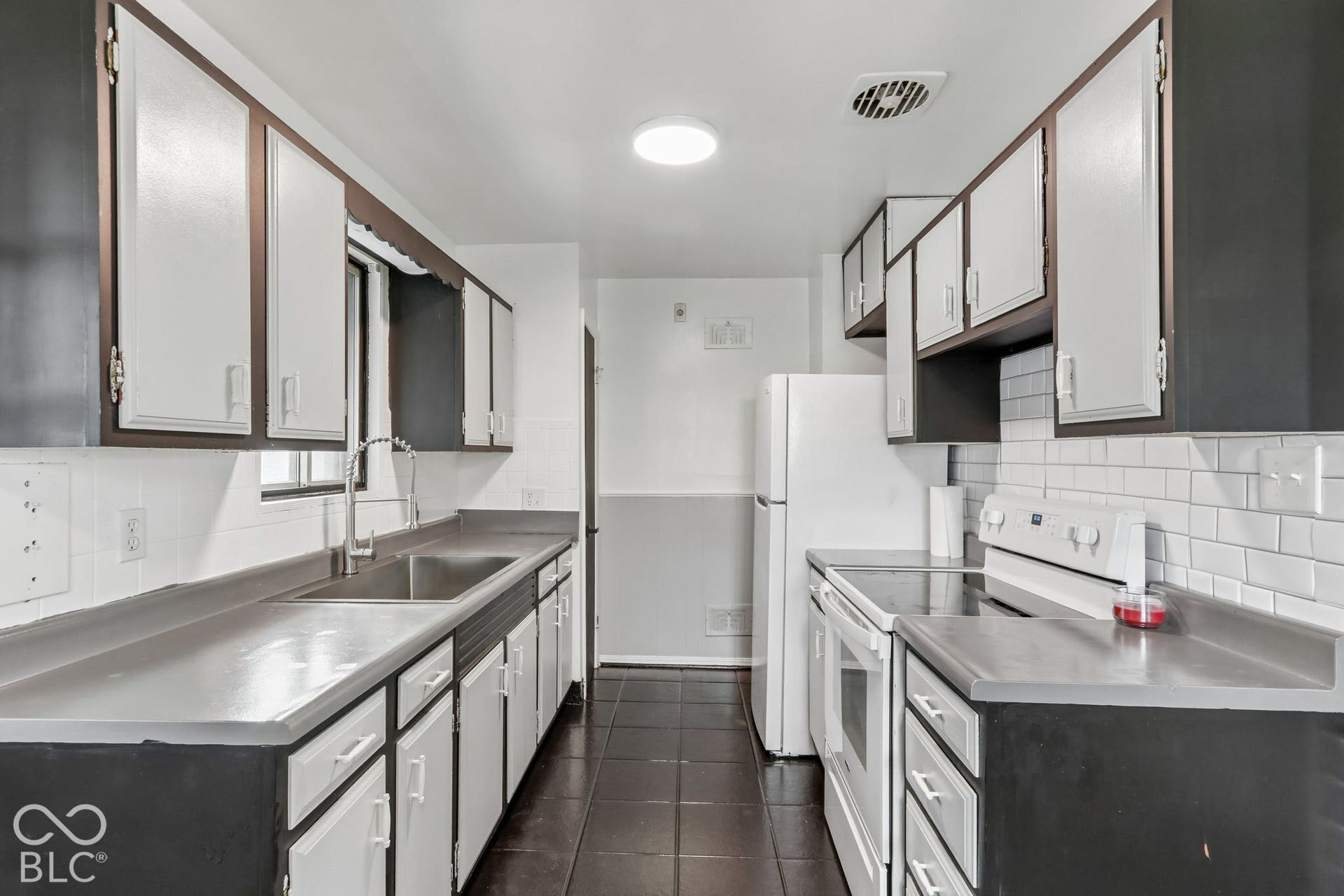 Kitchen featuring white subway tile backsplash, dark cabinetry with white panels, solid surface countertops, stainless steel undermount sink with arched pull-down faucet, and tiled flooring