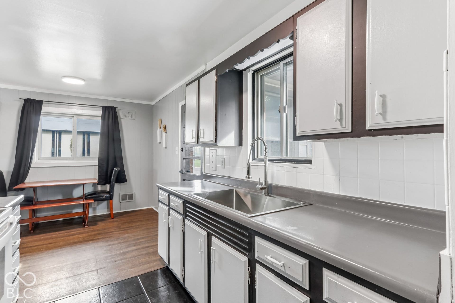 Kitchen featuring wood-finish flooring, shaker-style cabinetry with contrasting trim, a stainless steel undermount sink, a gooseneck faucet, and a tiled backsplash