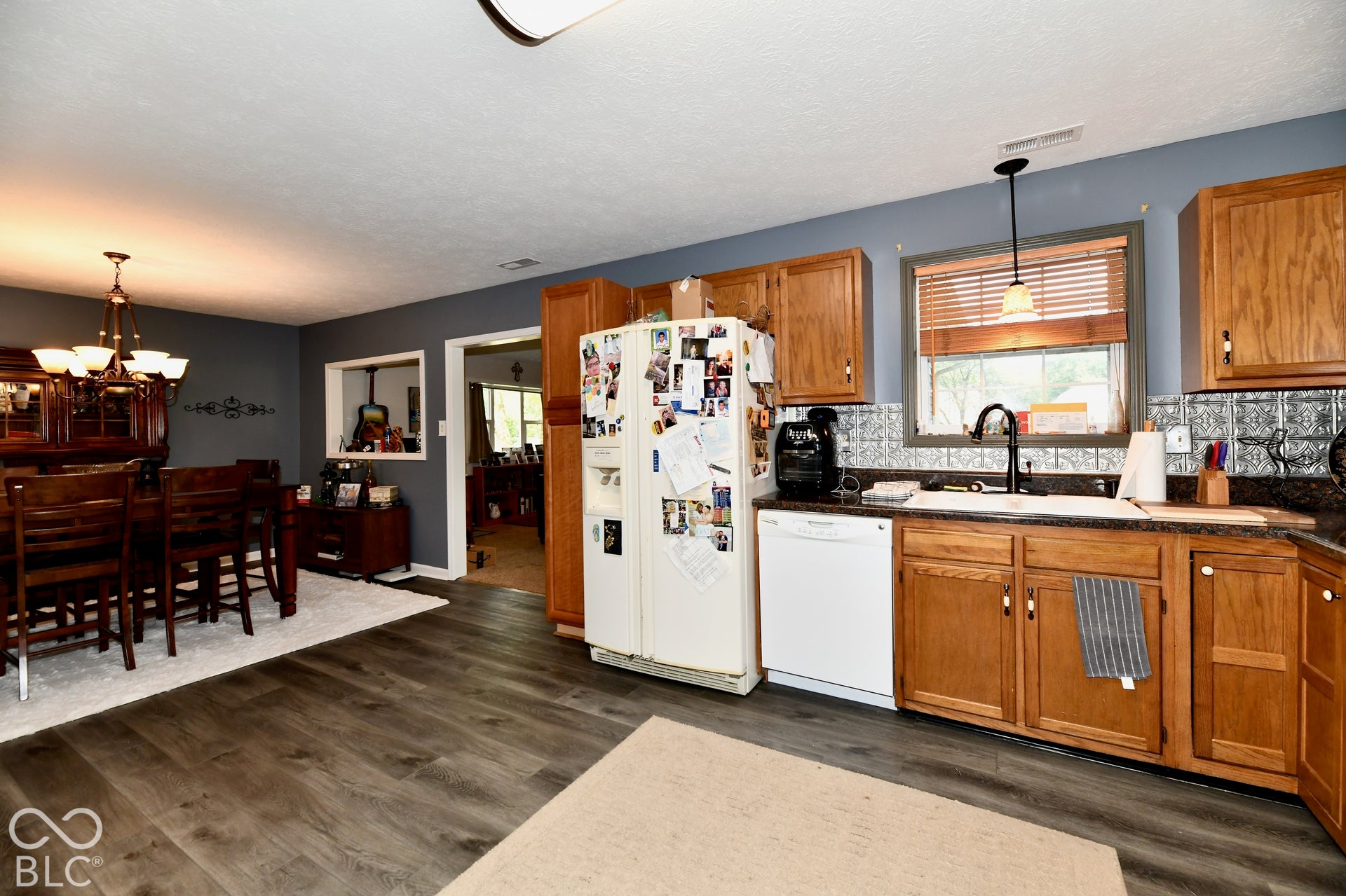 Kitchen featuring wood cabinetry, patterned tile backsplash, dark countertops, white farmhouse-style sink, and wood-finish flooring