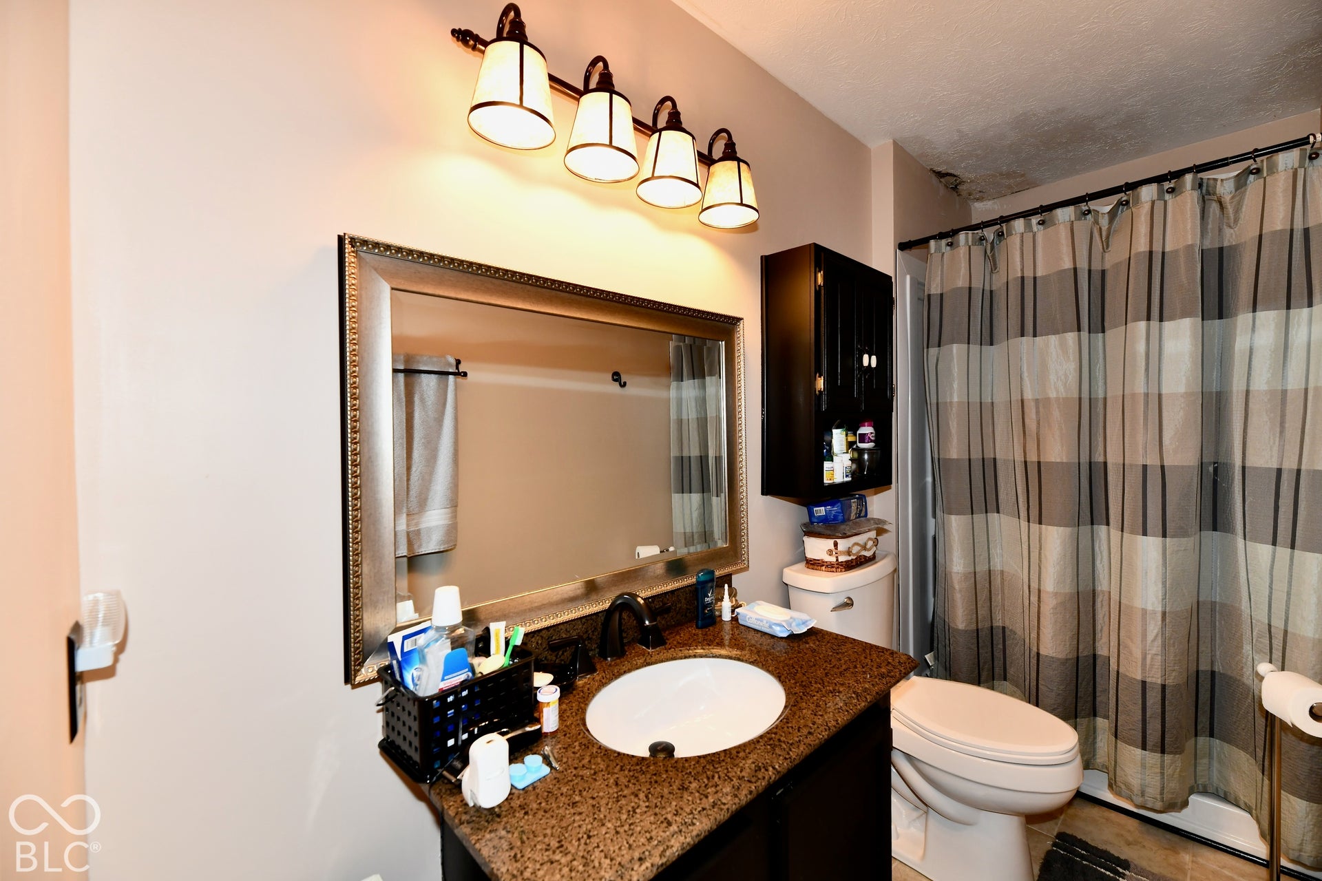 Bathroom vanity featuring a dark-finish base cabinet, stone-composite countertop with an integrated oval basin, wall-mounted four-light fixture, and framed vanity mirror with built-in wall cabinetry