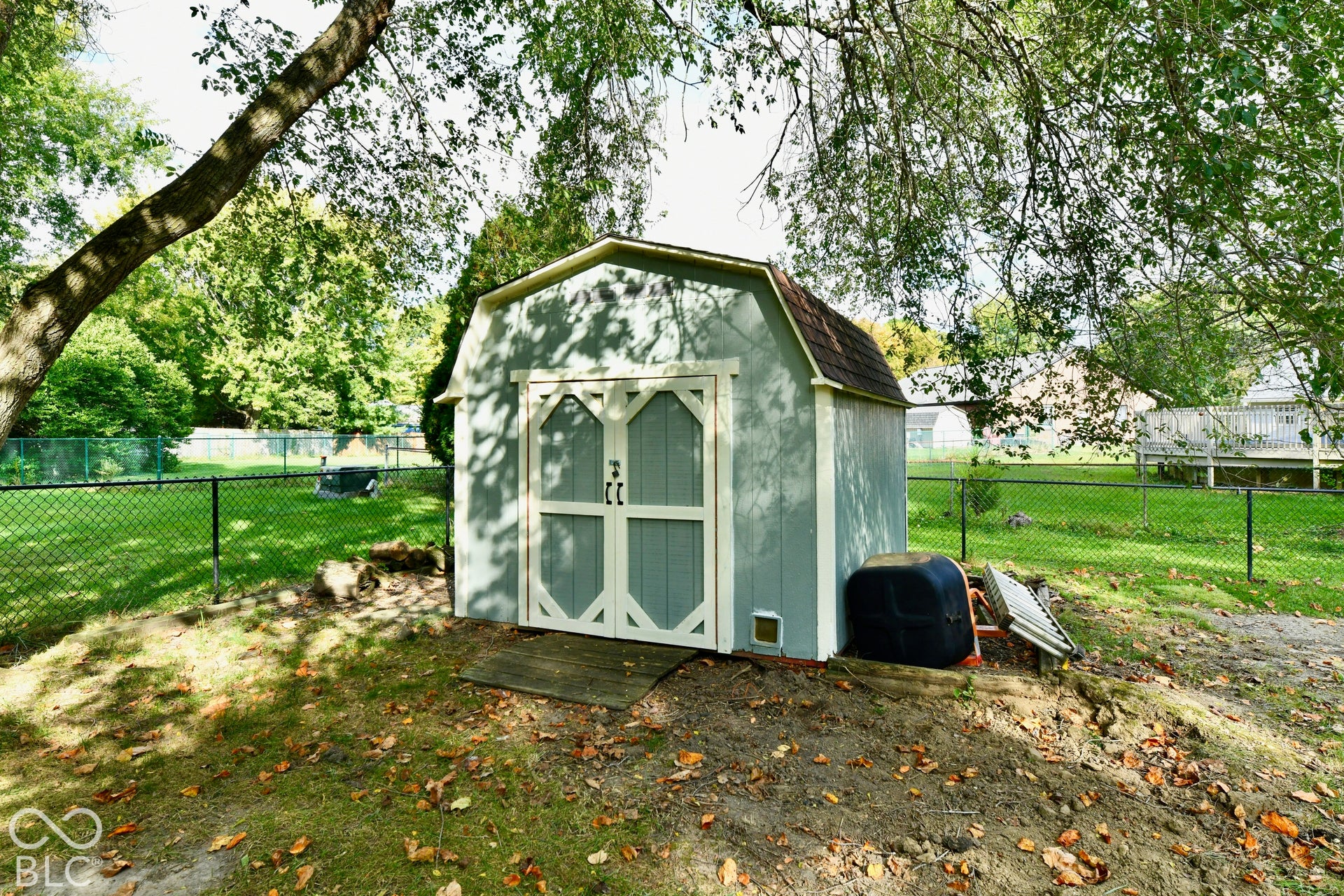 Barn-style exterior storage shed featuring double doors, shingled roofing, and a fenced backyard