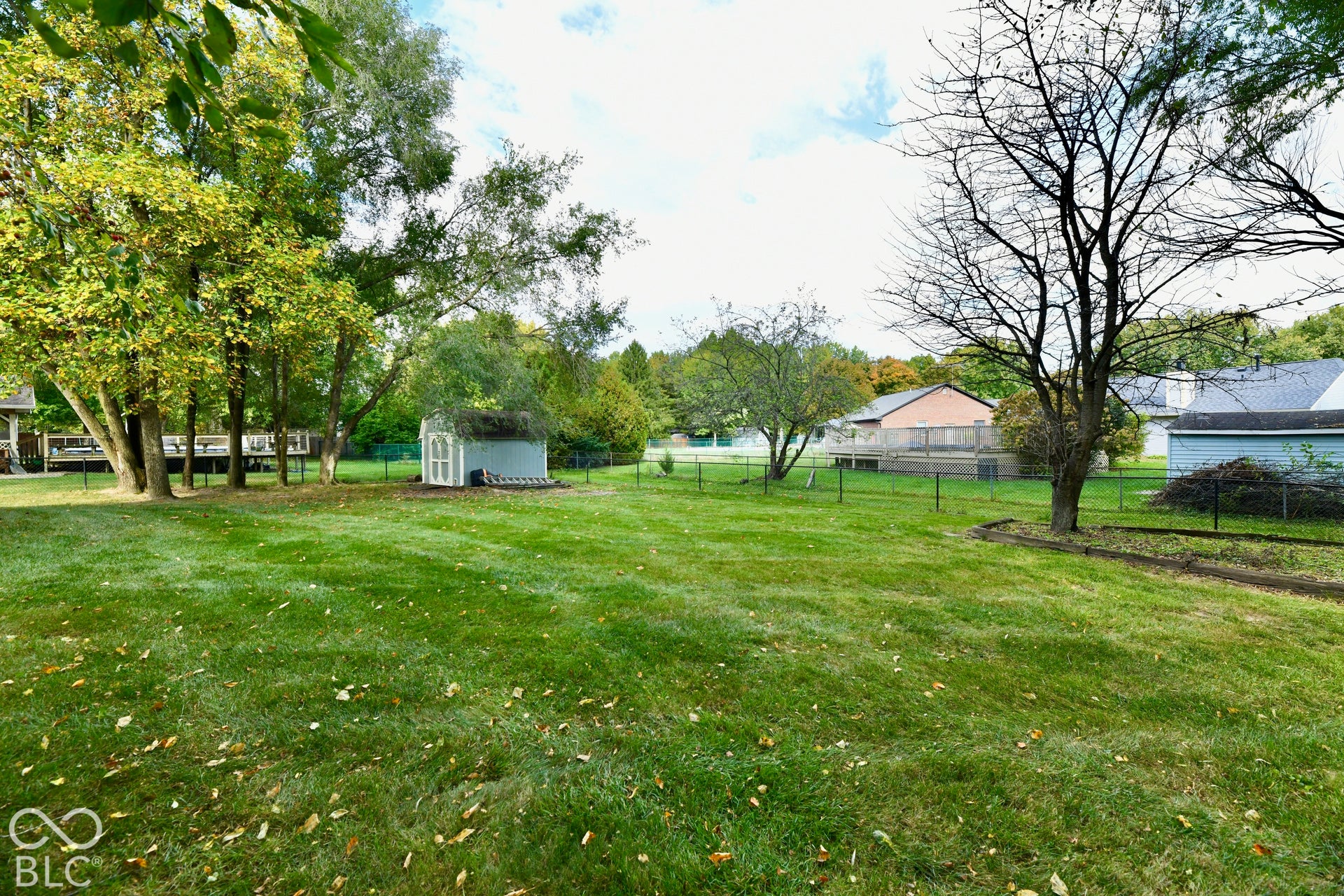 Expansive backyard featuring a level lawn, mature trees, a detached storage shed, and perimeter chain-link fencing