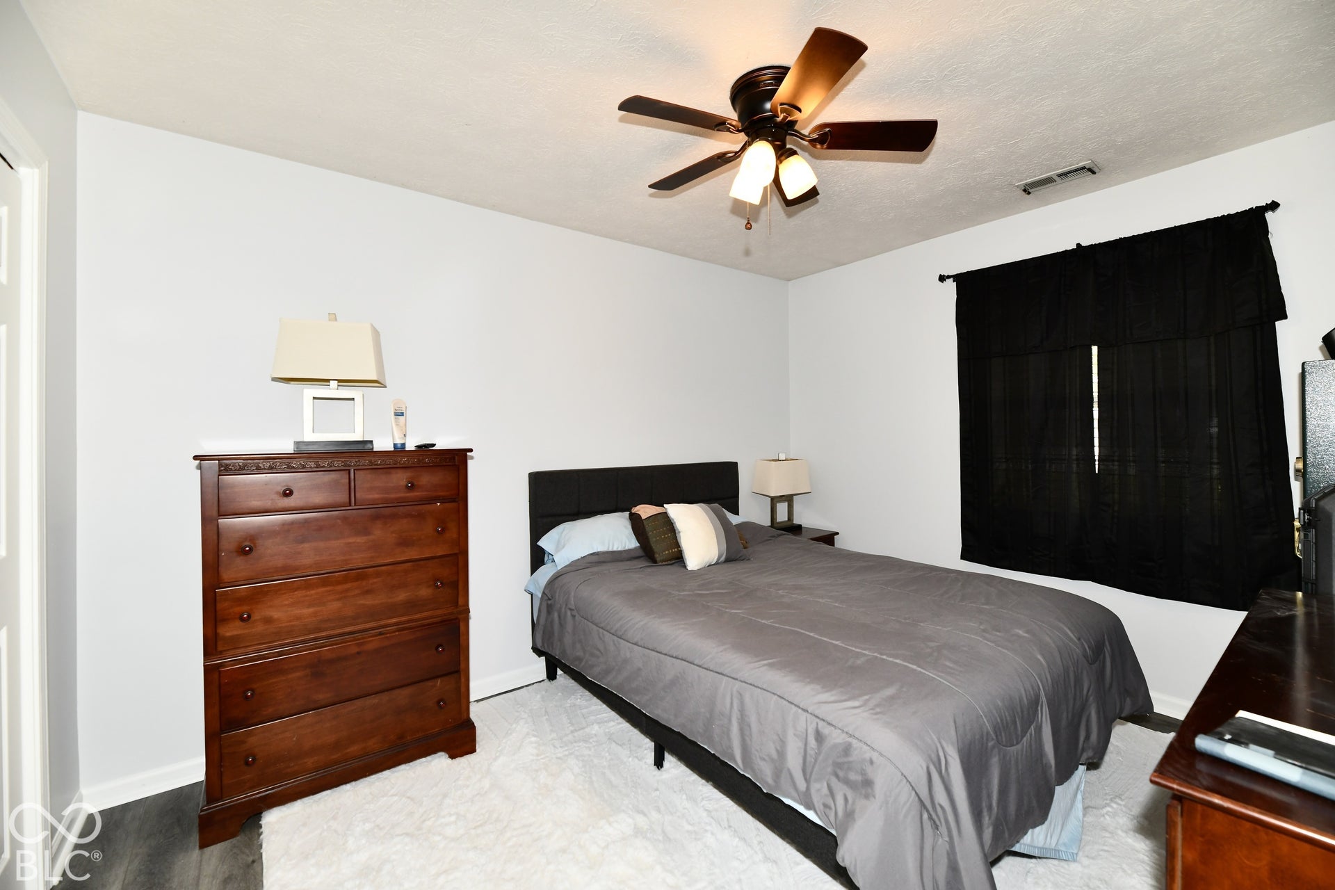 Neutral-toned interior room featuring wood-finish flooring and a multi-blade ceiling fan with integrated lighting