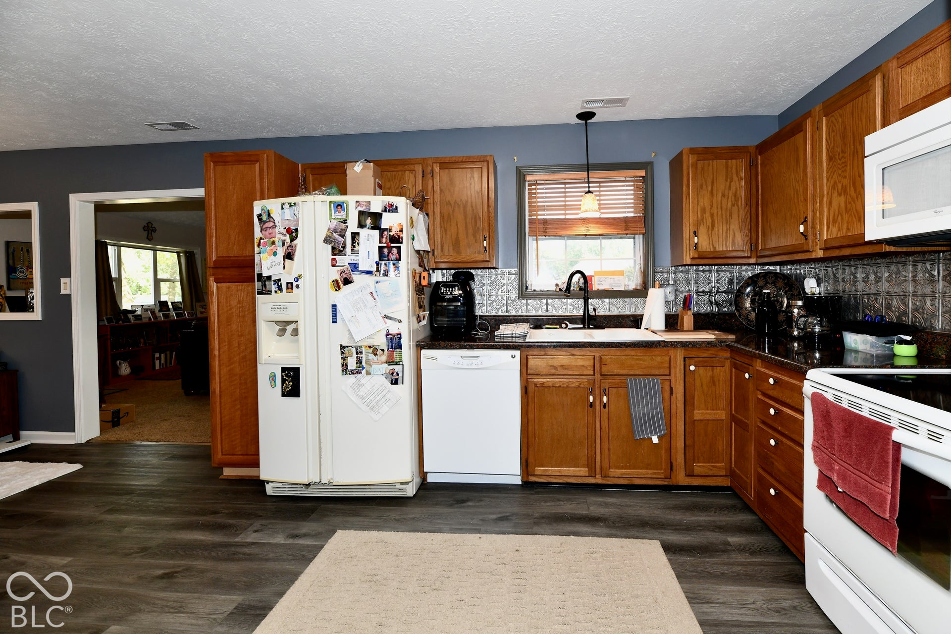 Kitchen featuring wood cabinetry, patterned tile backsplash, wood-finish flooring, dark stone countertops, and a white farmhouse-style sink with a matte black faucet